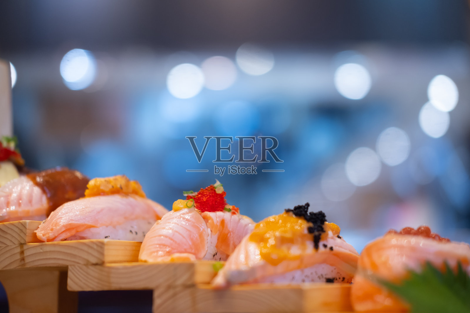 寿司不同的三文鱼套餐在木踏板托盘上与模糊的灯光背景。日本料理。照片摄影图片