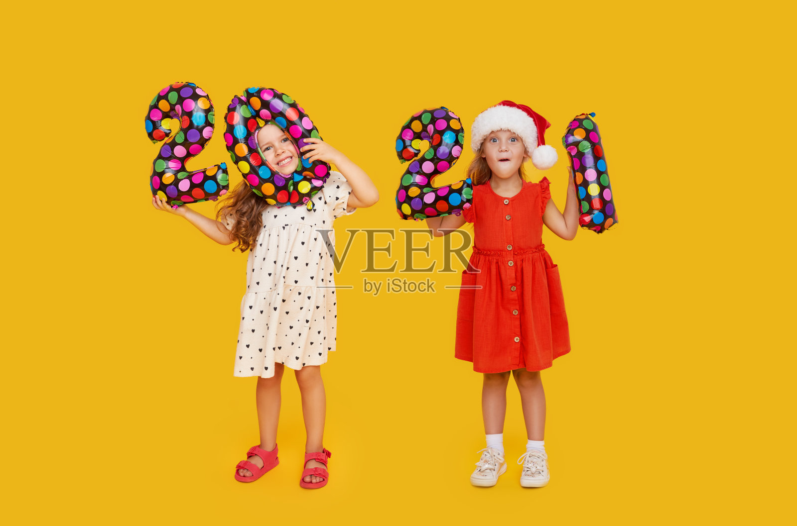 兴高采烈的孩子们戴着圣诞帽，黄色背景上写着彩色数字2021。气球新年派对快乐照片摄影图片