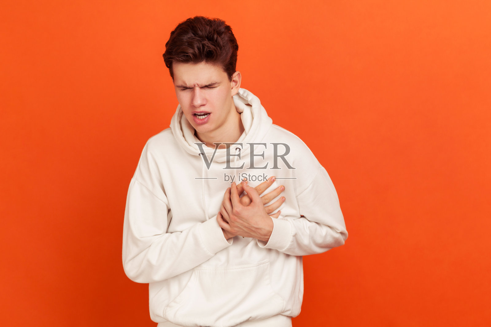 焦虑悲伤的青少年穿着休闲连帽衫，手放在胸前，感到心脏剧痛，有心脏病发作的风险照片摄影图片