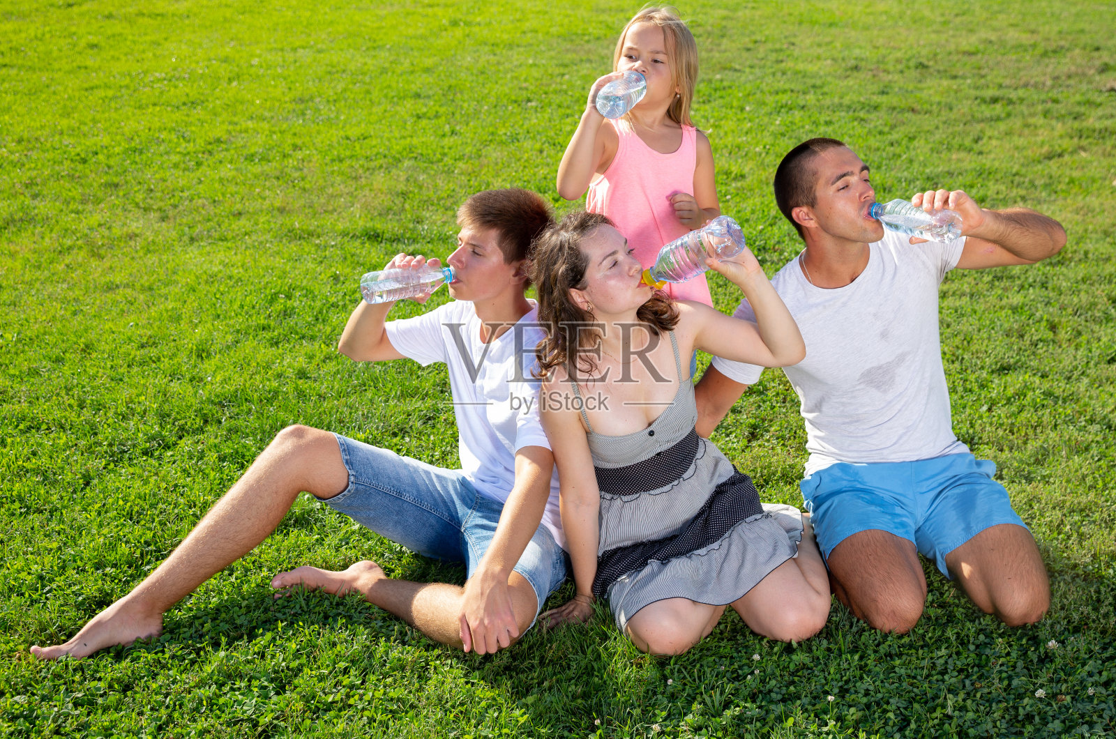 父母带着十几岁的儿子和女儿在夏季公园喝塑料瓶里的冷水照片摄影图片