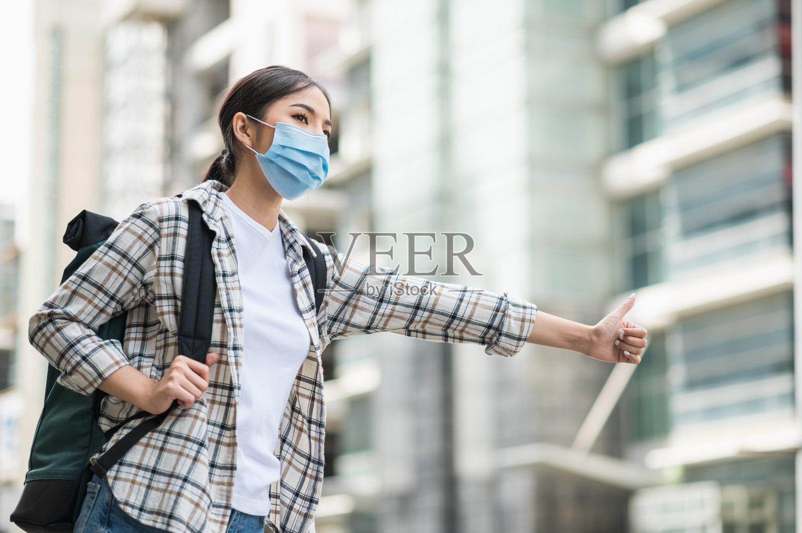 年轻美丽的亚洲女子背包旅行在城市和搭便车戴口罩，以保护病毒安全旅行。照片摄影图片