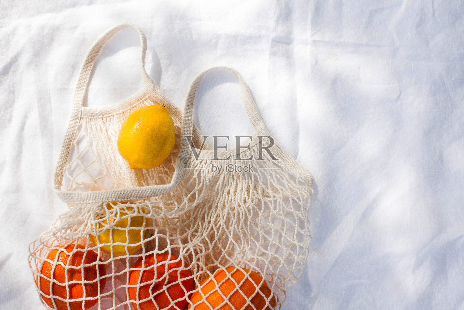 白色桌布上，阳光下挂着一袋多汁的柑橘类水果。健康的饮食习惯。维生素。副本的空间。照片摄影图片