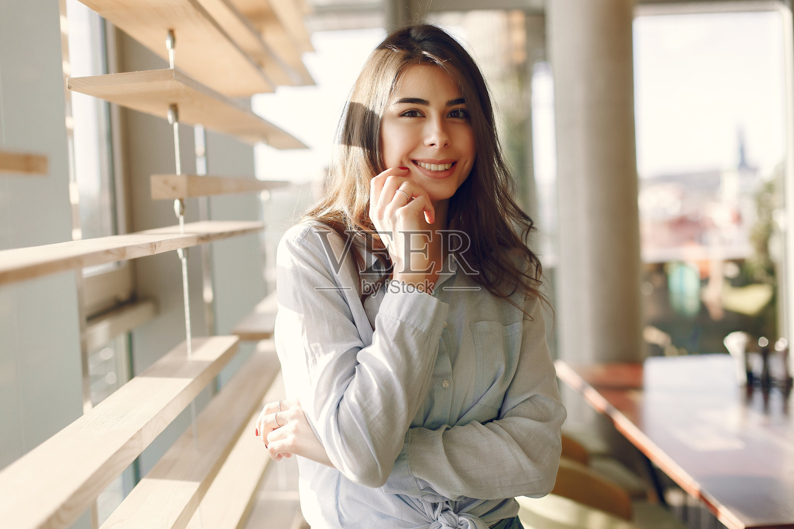 微笑的女孩在一个蓝色的衬衫站在窗口和摆姿势照片摄影图片