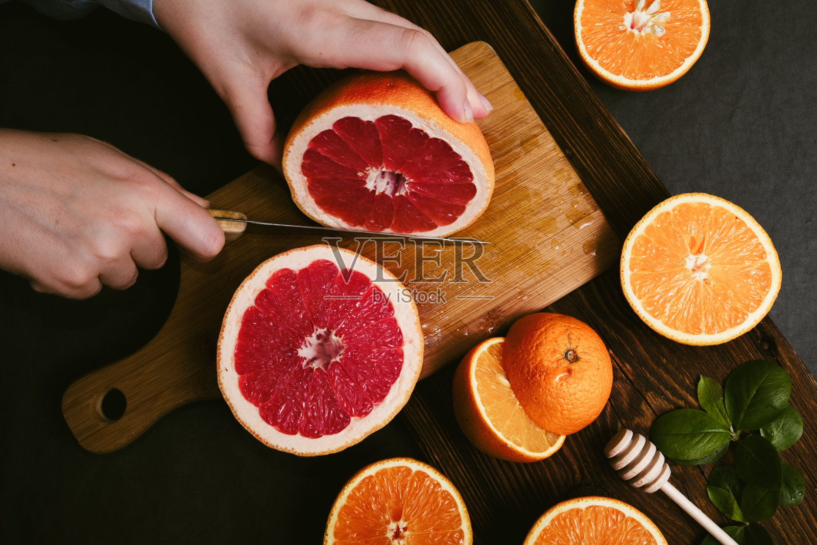 手在木板上切成两半的新鲜橙子和葡萄柚的俯视图。柑橘类水果深色背景。照片摄影图片
