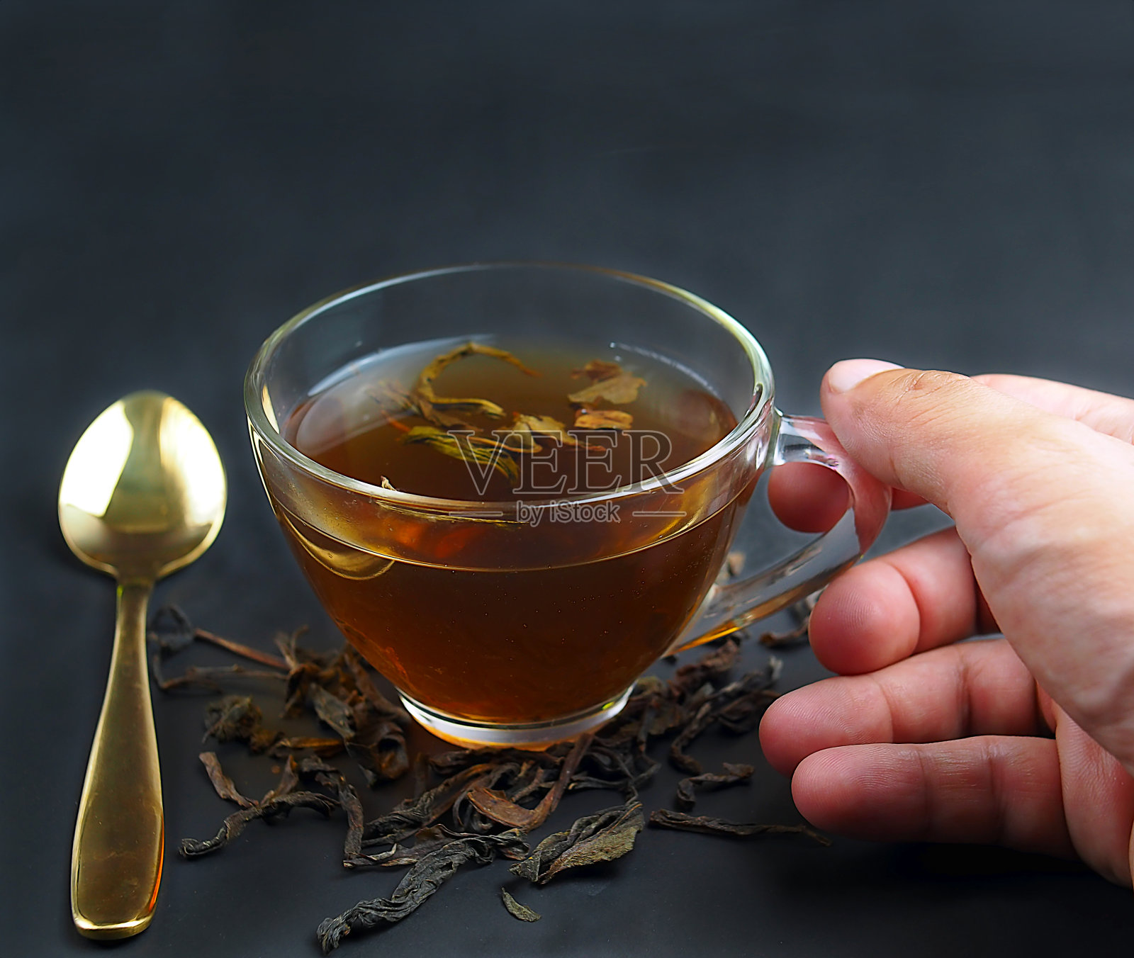 右手拿着一杯茶和勺子在黑色的背景照片摄影图片