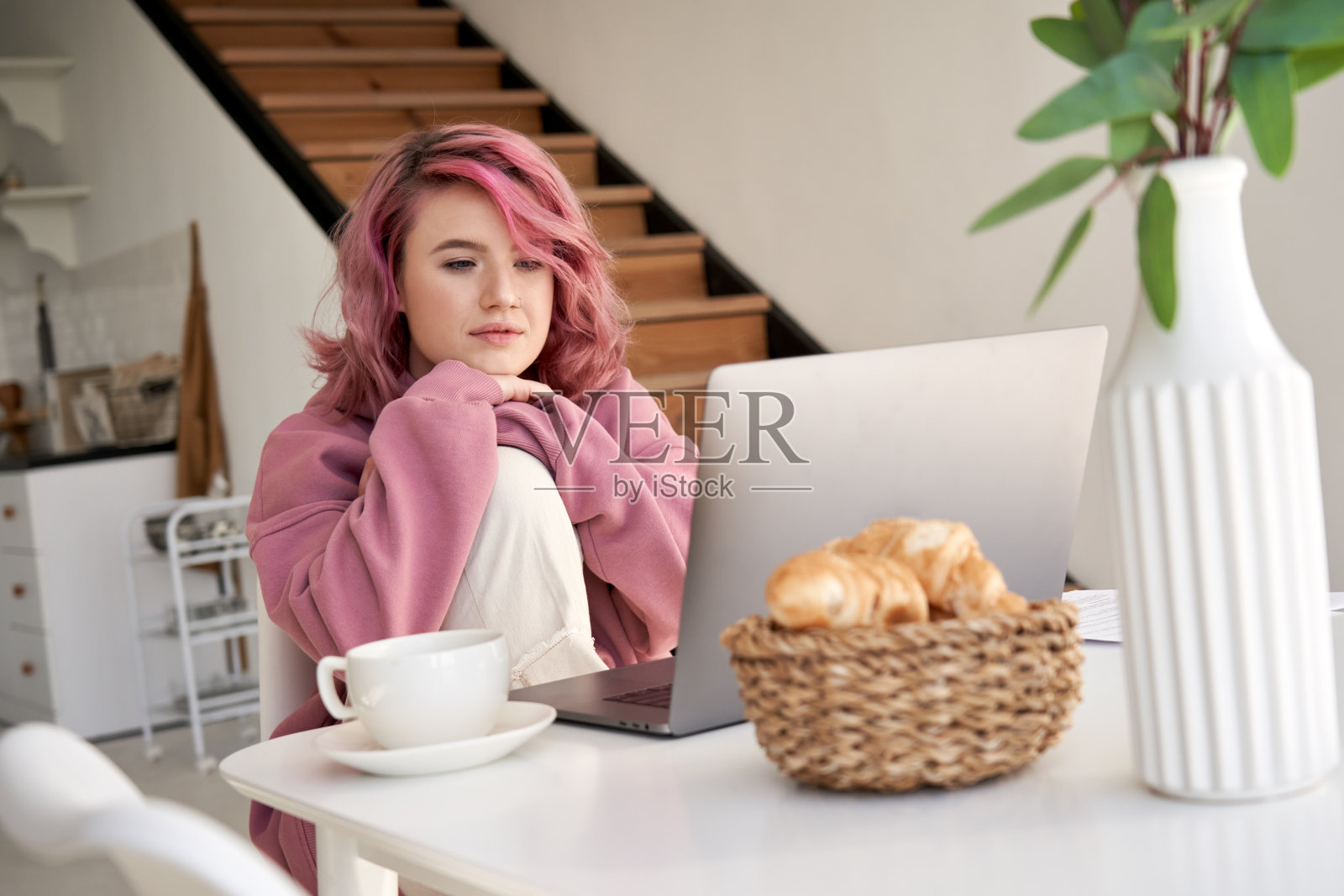 粉色头发的年轻时髦女孩坐在餐桌前看视频。照片摄影图片