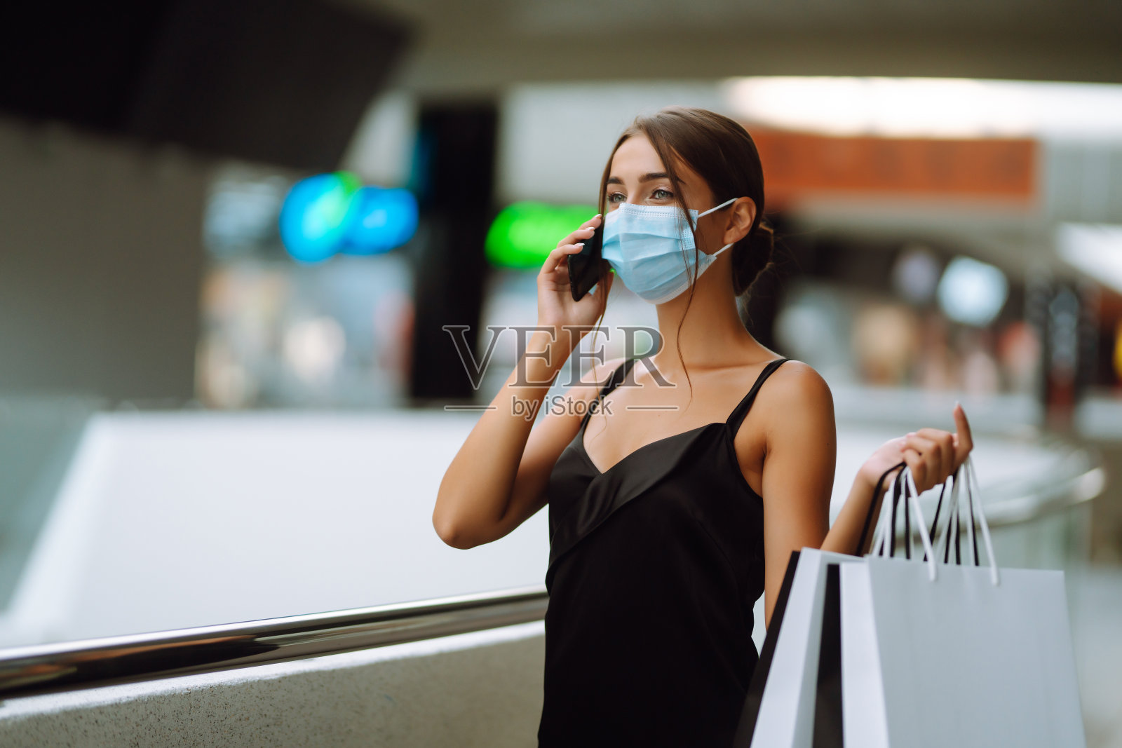 一名穿着黑色连衣裙的年轻女子正在打手机。Covid - 2019。照片摄影图片