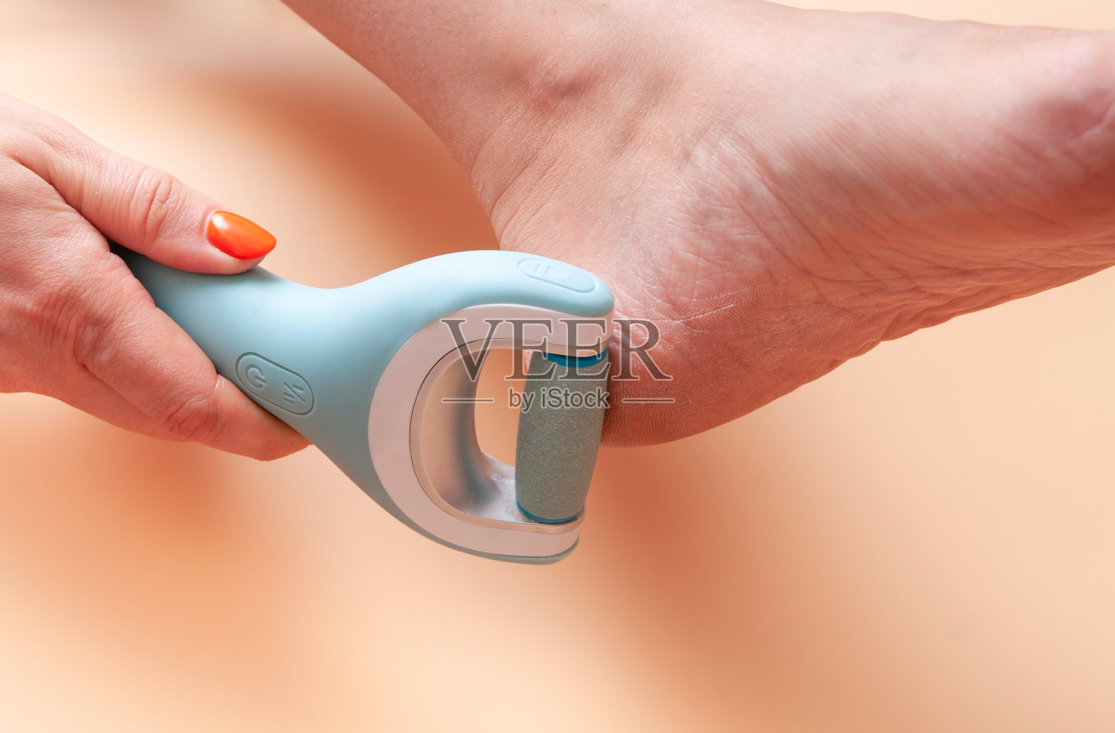 护理和清洁女人的脚从粗糙，鳞片皮肤。一种电动脚死皮去除器，在妇女家里磨脚后跟。照片摄影图片