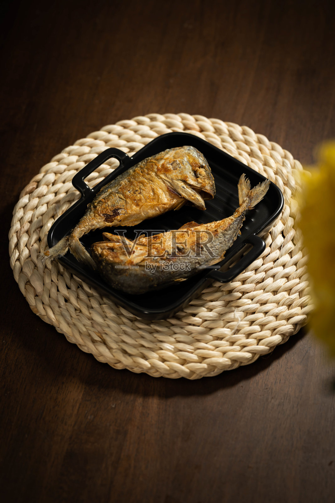 泰国食品，两炸薯条短鲭鱼放置在一个黑色的容器或平底锅上，在手工编织的餐垫和一个黑色的木桌上照片摄影图片