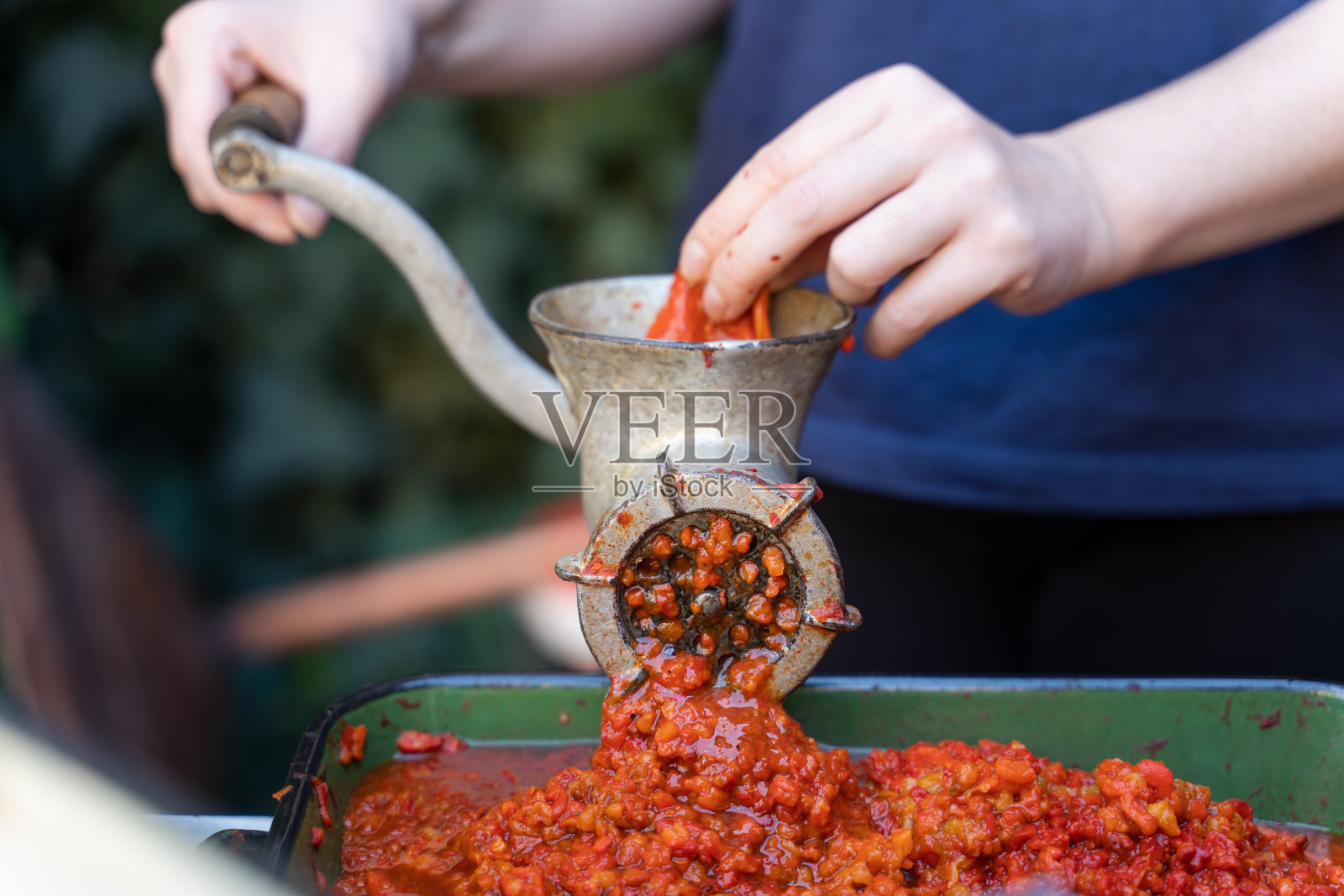 关闭户外女性的手在蔬菜研磨机准备红辣椒烤红辣椒为ajvar民族菜在巴尔干-健康有机食品的概念照片摄影图片