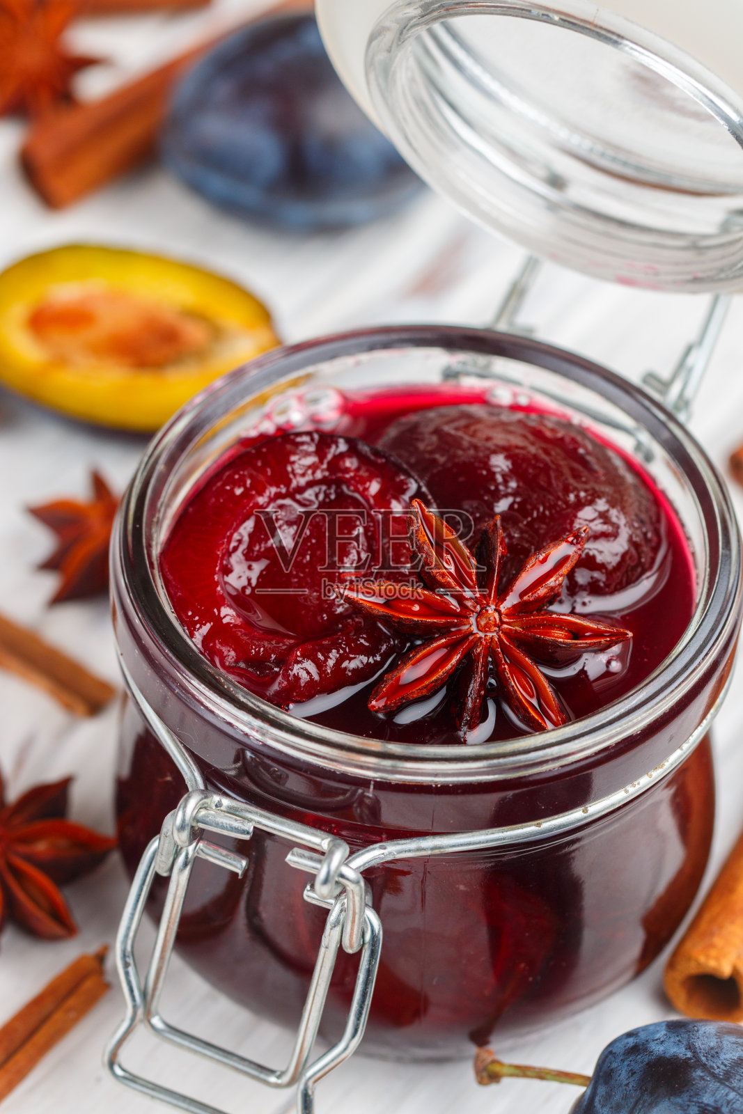 瓶自制李子果酱，肉桂和八角在白色木制背景特写。桌上放着新鲜的水果和香料。有选择性的重点照片摄影图片