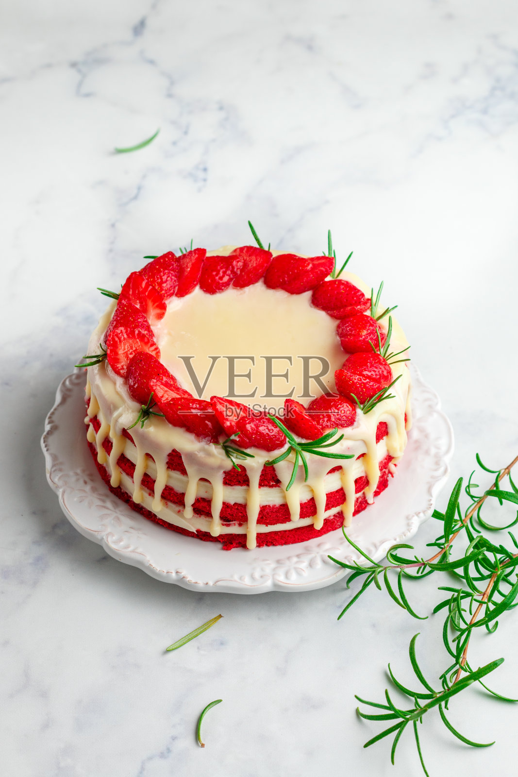 自制红丝绒蛋糕配白巧克力，新鲜草莓和迷迭香。美味的美食甜点在一个白色盘子上的大理石表面特写。选择性聚焦，复制空间照片摄影图片