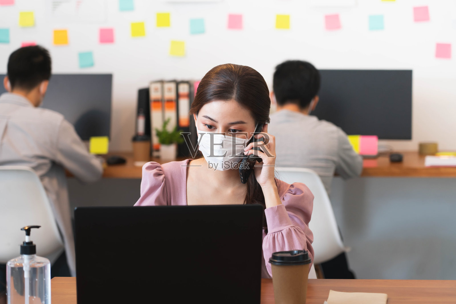 选择性聚焦年轻美丽的亚洲商务女性，戴着防护口罩打电话，以新的正常生活方式在办公室工作，以预防covid-19感染。照片摄影图片