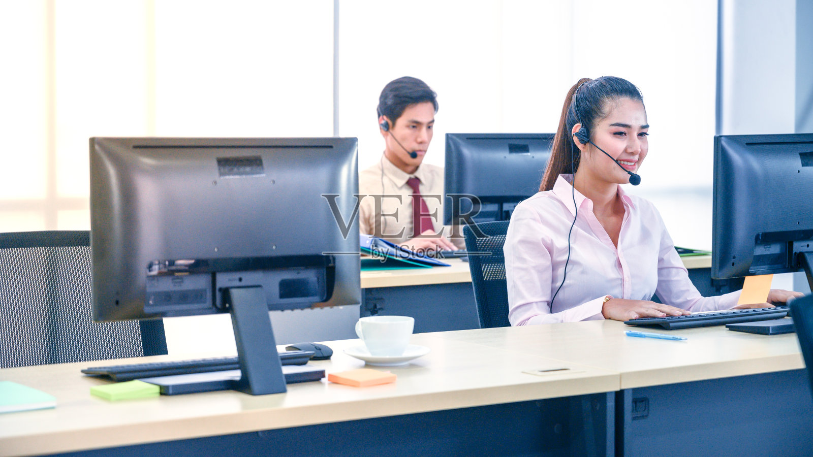 年轻的女客户服务代理，戴着耳机和电脑在办公室工作。照片摄影图片