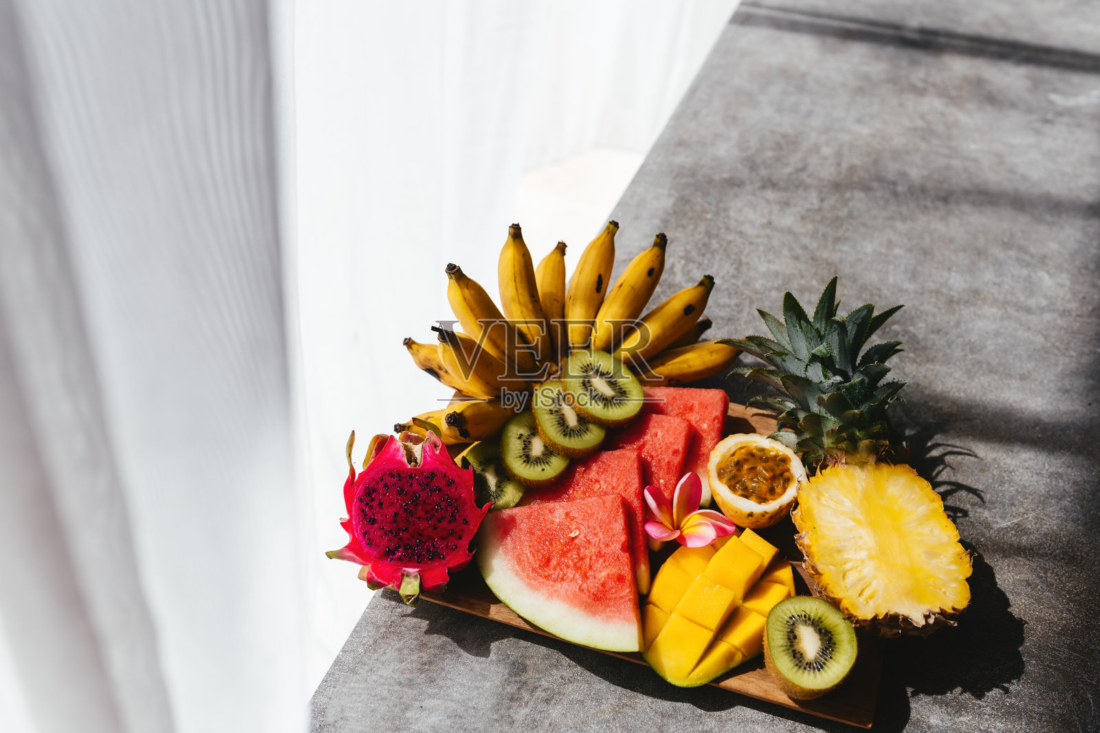 木盘上各种各样的热带水果。石头的背景。照片摄影图片