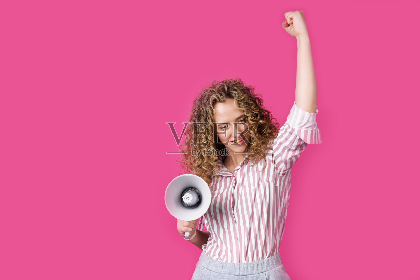 一名年轻女子手持扩音器，表达获胜者的情绪。孤立的粉色背景。照片摄影图片