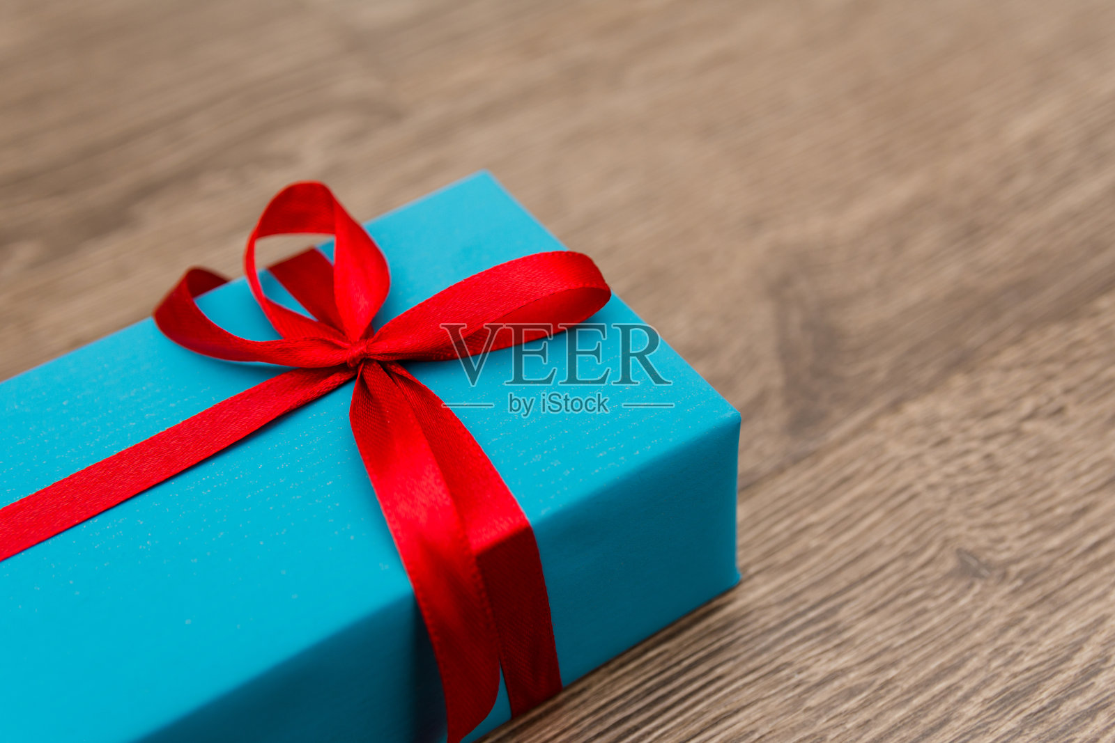 木制背景上放着一台智能手机，盒子是蓝色的，上面系着红色的丝带。一件包装精美的假日礼物。这是在爱的人生日时关心他们的标志。照片摄影图片