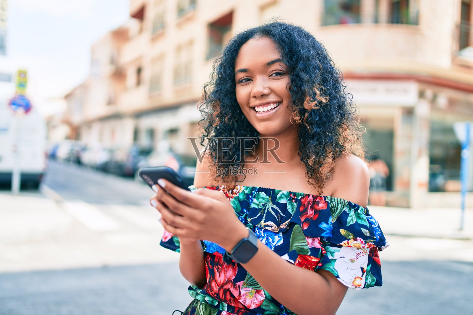 年轻的非洲裔美国妇女与卷曲的头发微笑快乐的户外使用智能手机照片摄影图片