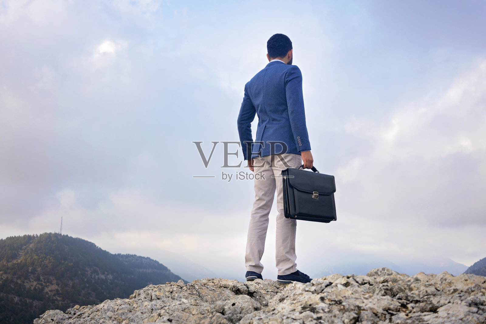 年轻的商人站在山顶，头顶乌云。照片摄影图片