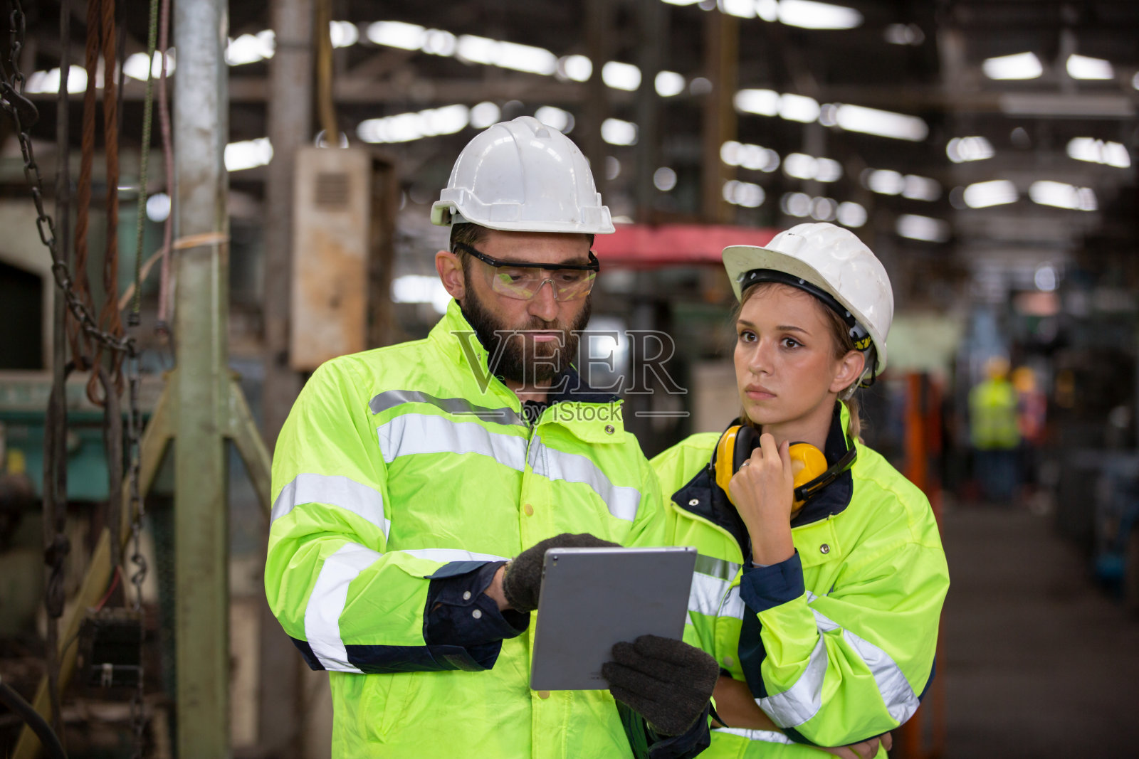 两位工业工程师在使用笔记本电脑时与工厂工人交谈。他们在重工业制造工厂工作。照片摄影图片
