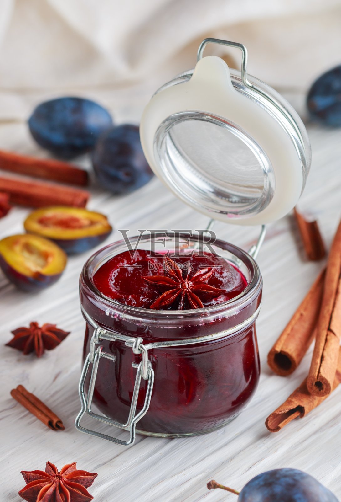 将自制的梅子果酱、肉桂和八角放在白色的木质背景上。桌上放着新鲜的水果和香料。有选择性的重点照片摄影图片