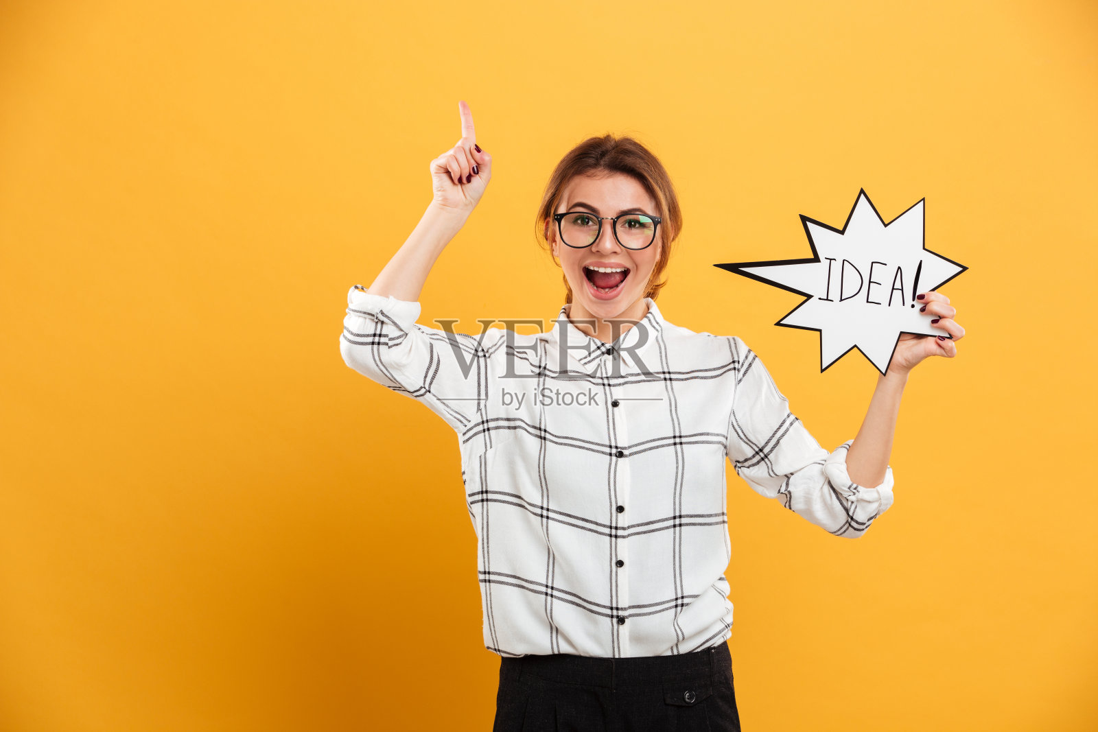 一个积极的女人穿着格子衬衫举着演讲泡泡，手指向上，孤立在黄色的背景下照片摄影图片