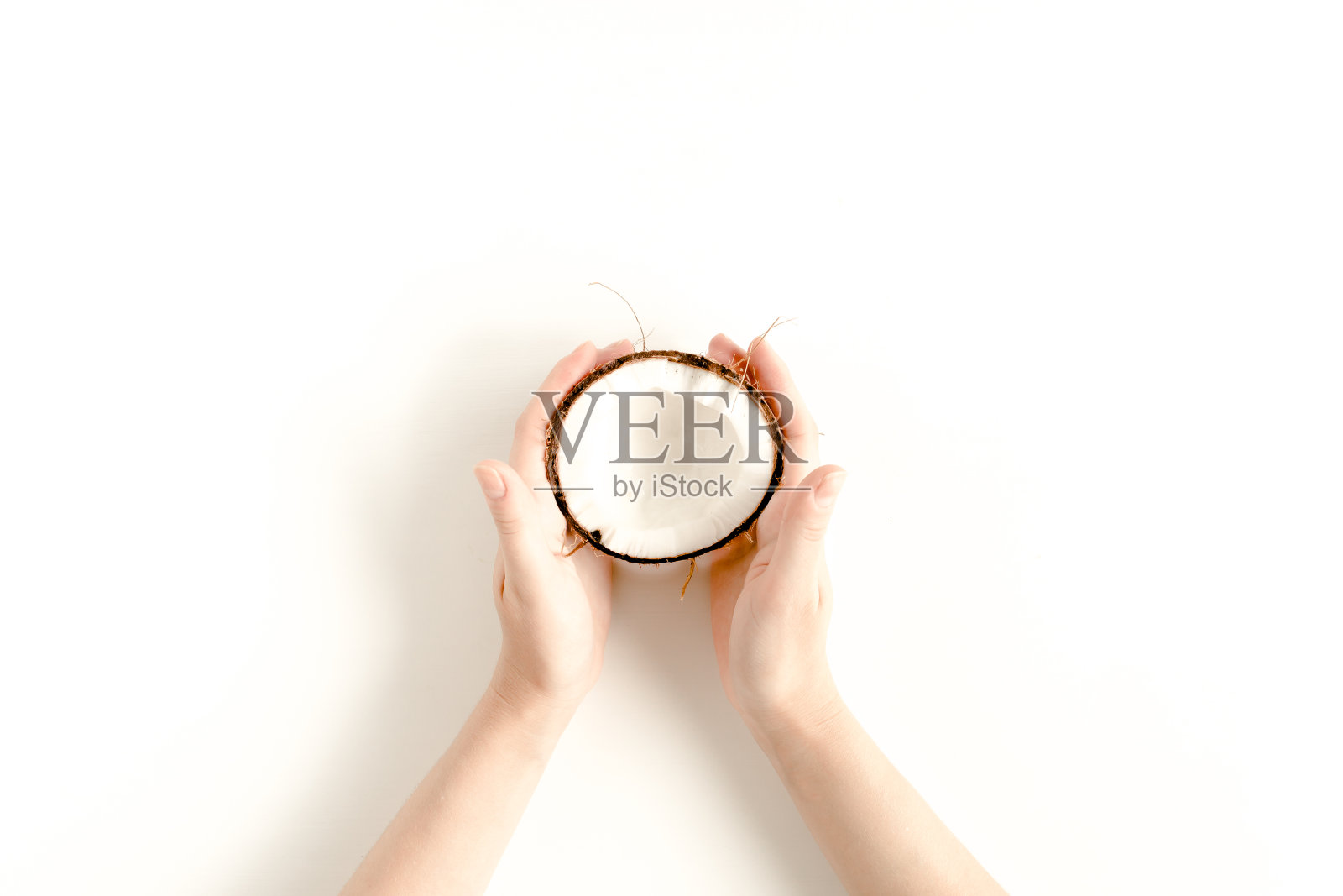 女人的手拿着一半椰子在白色的背景。平躺，俯视图照片摄影图片