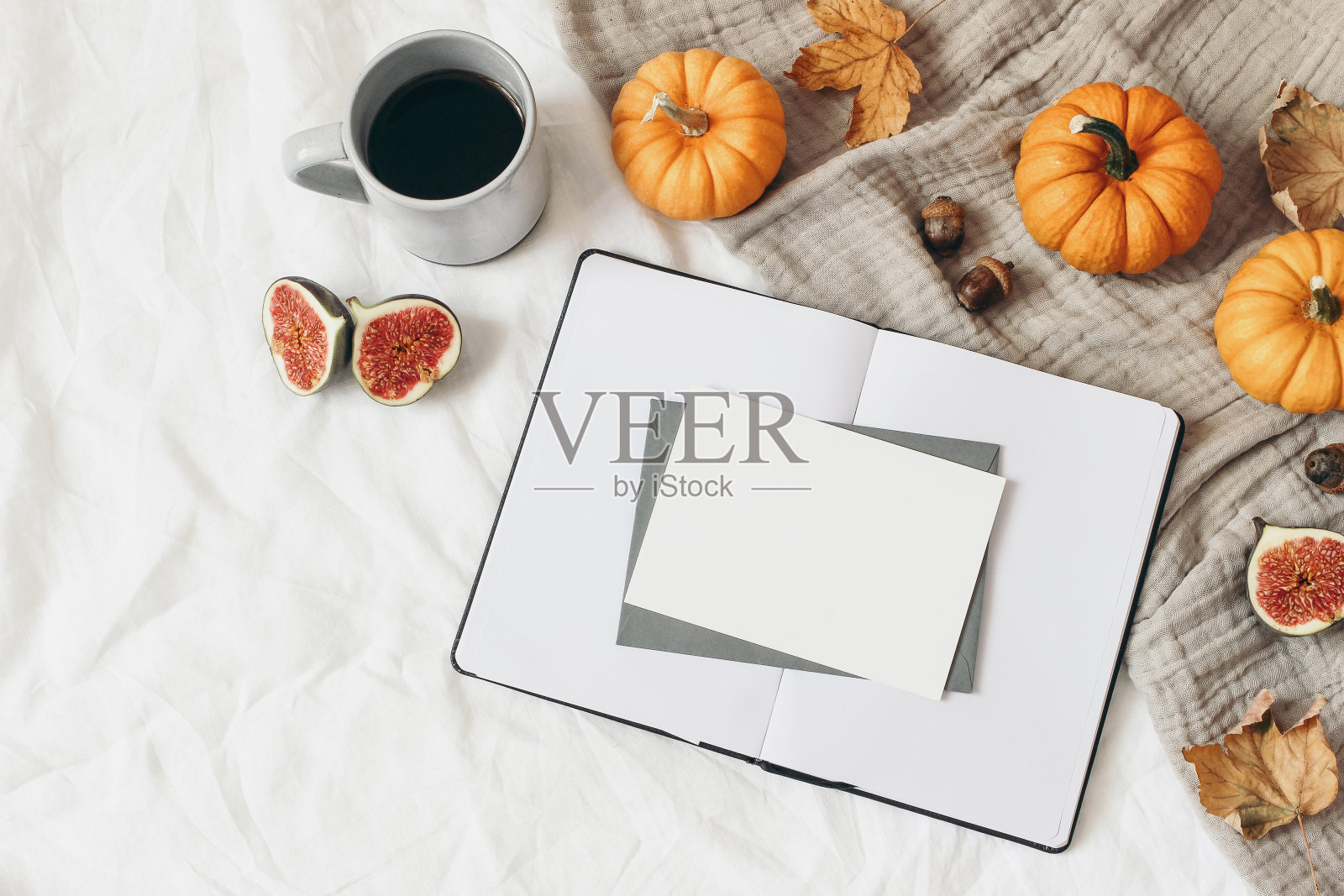 秋天的早餐组合。空打开笔记本。贺卡模型。一杯咖啡，五颜六色的叶子，无花果和橙色的南瓜。白色亚麻的背景。感恩节,万圣节。平躺，俯视图。照片摄影图片