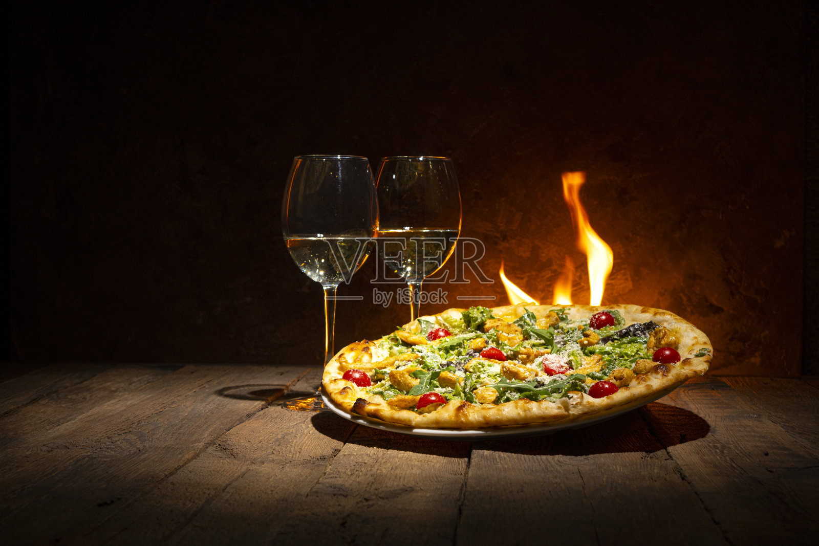 一份刚从炉子里拿出来的美味披萨，还有两个酒杯放在靠火的木桌上照片摄影图片