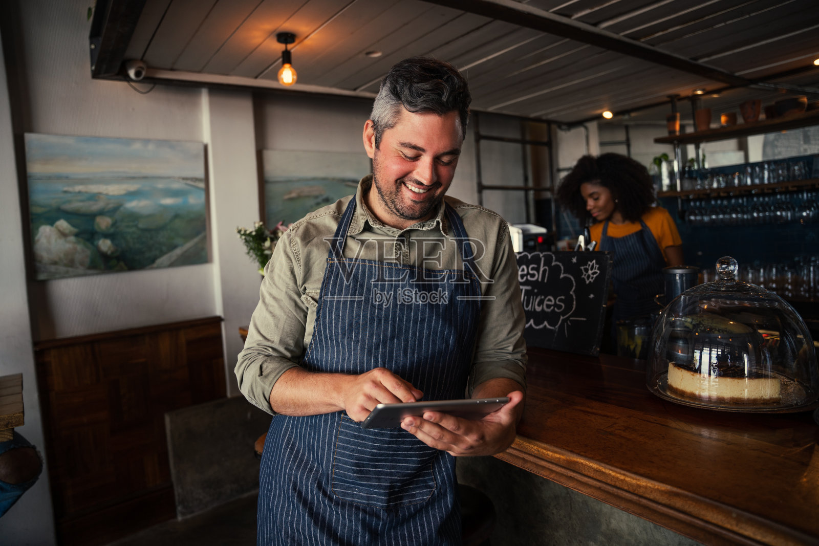 英俊和微笑的男性咖啡店老板浏览平板电脑在咖啡店照片摄影图片
