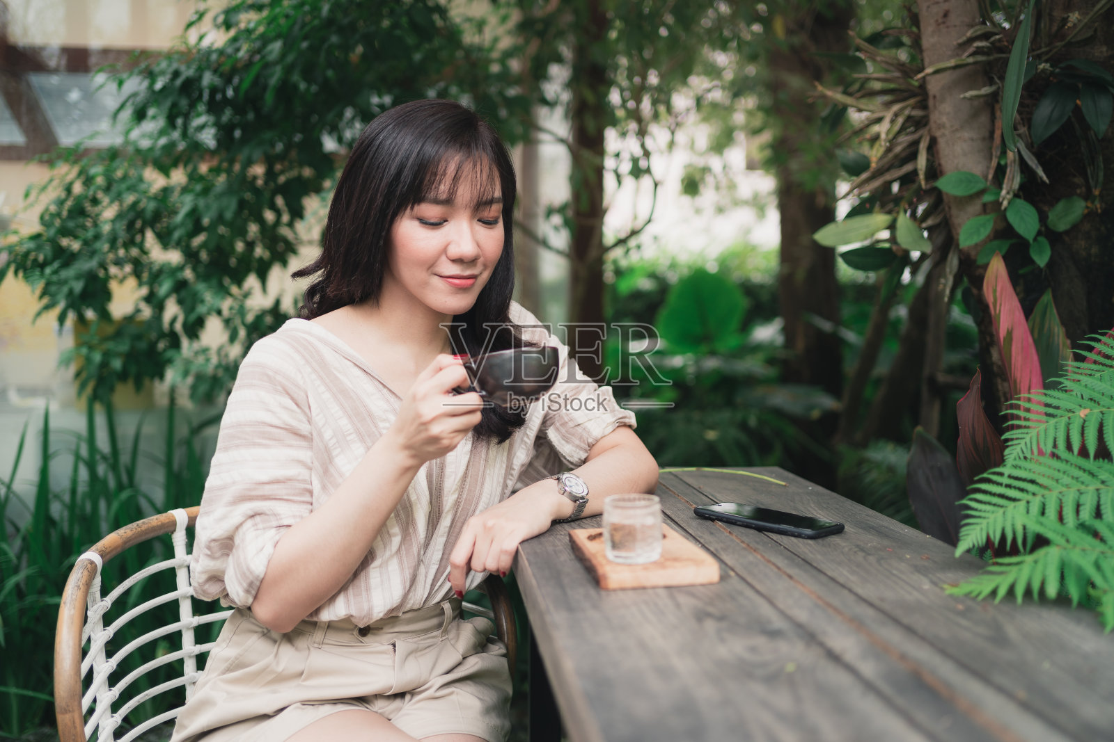 年轻的亚洲女人放松在花园与一杯咖啡在早上。一个女人吸入了咖啡照片摄影图片