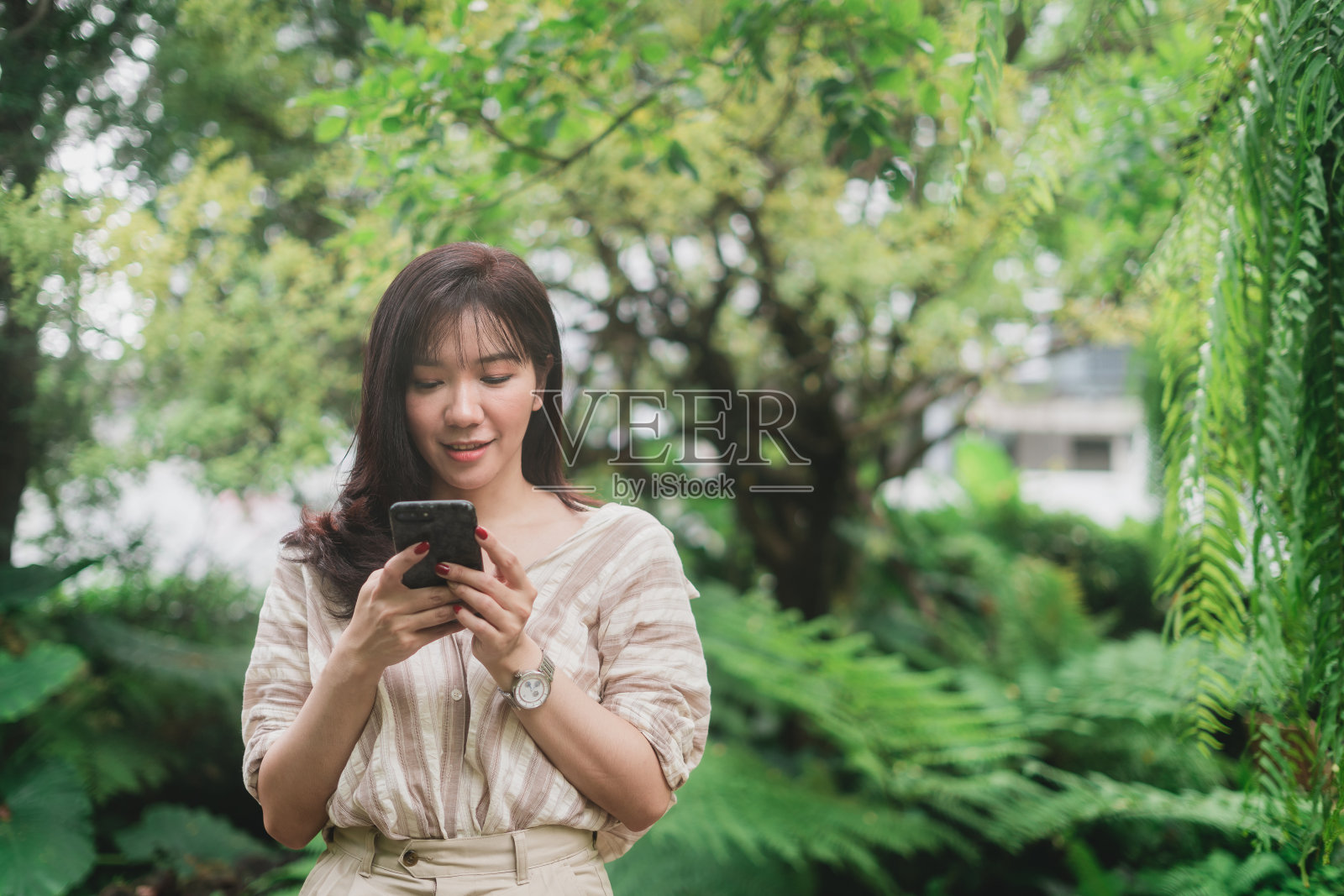 年轻的亚洲女性用智能手机聊天或搜索信息。一个女人在绿色的花园里有一个笑脸照片摄影图片