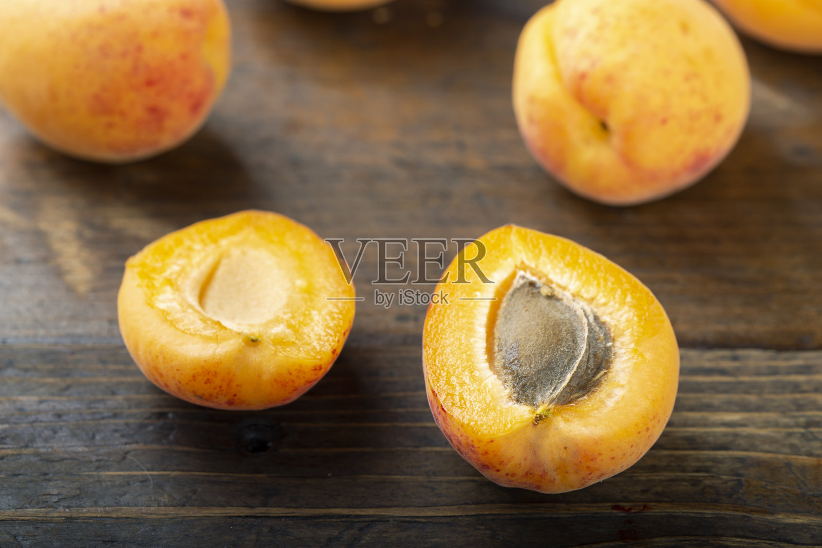 木制背景上的成熟有机杏。前景是半颗杏和果核。照片摄影图片