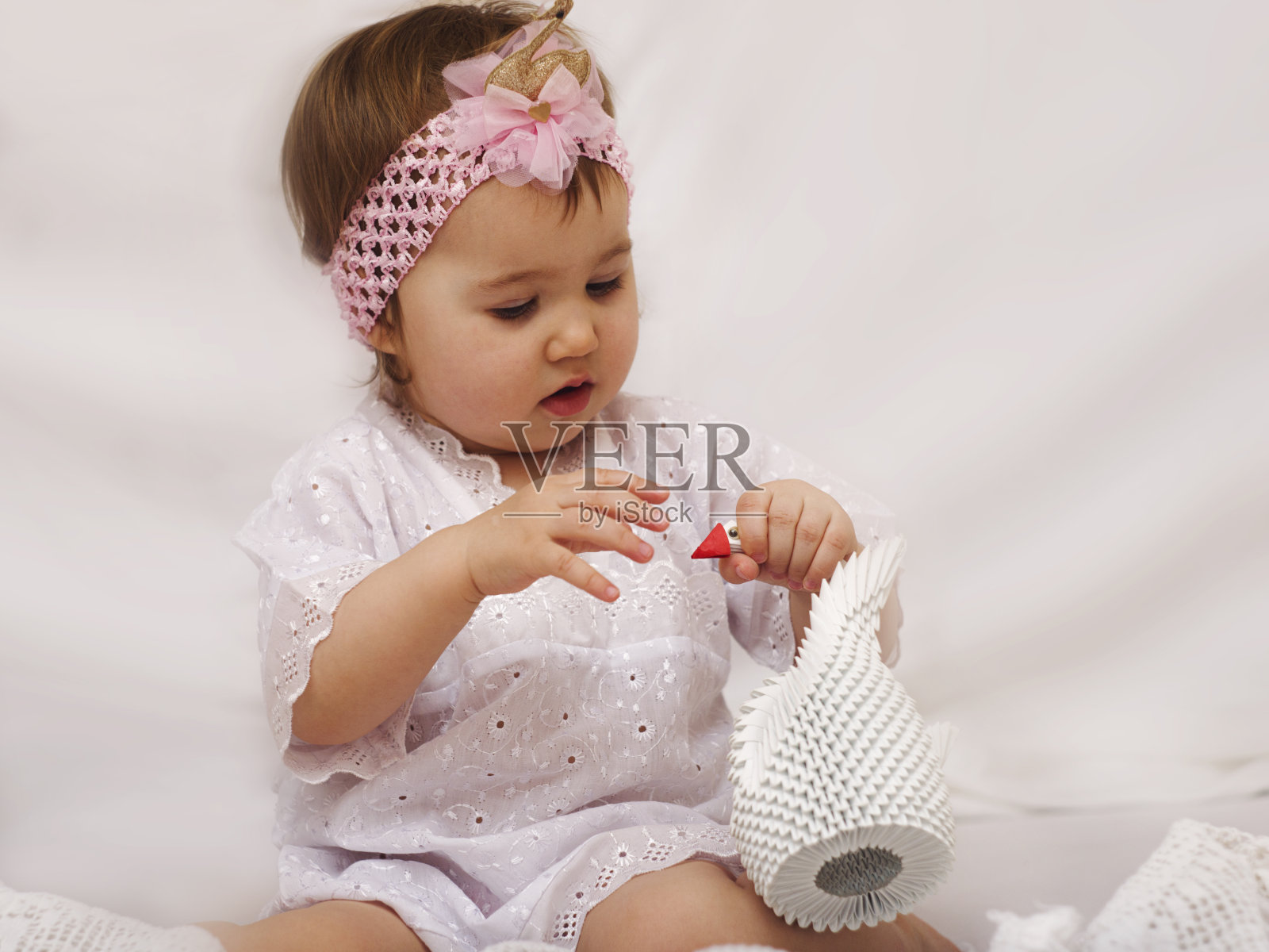 一个穿着白色镂空衬衫的婴儿正拿着一只白色的折纸天鹅。光的关键。照片摄影图片