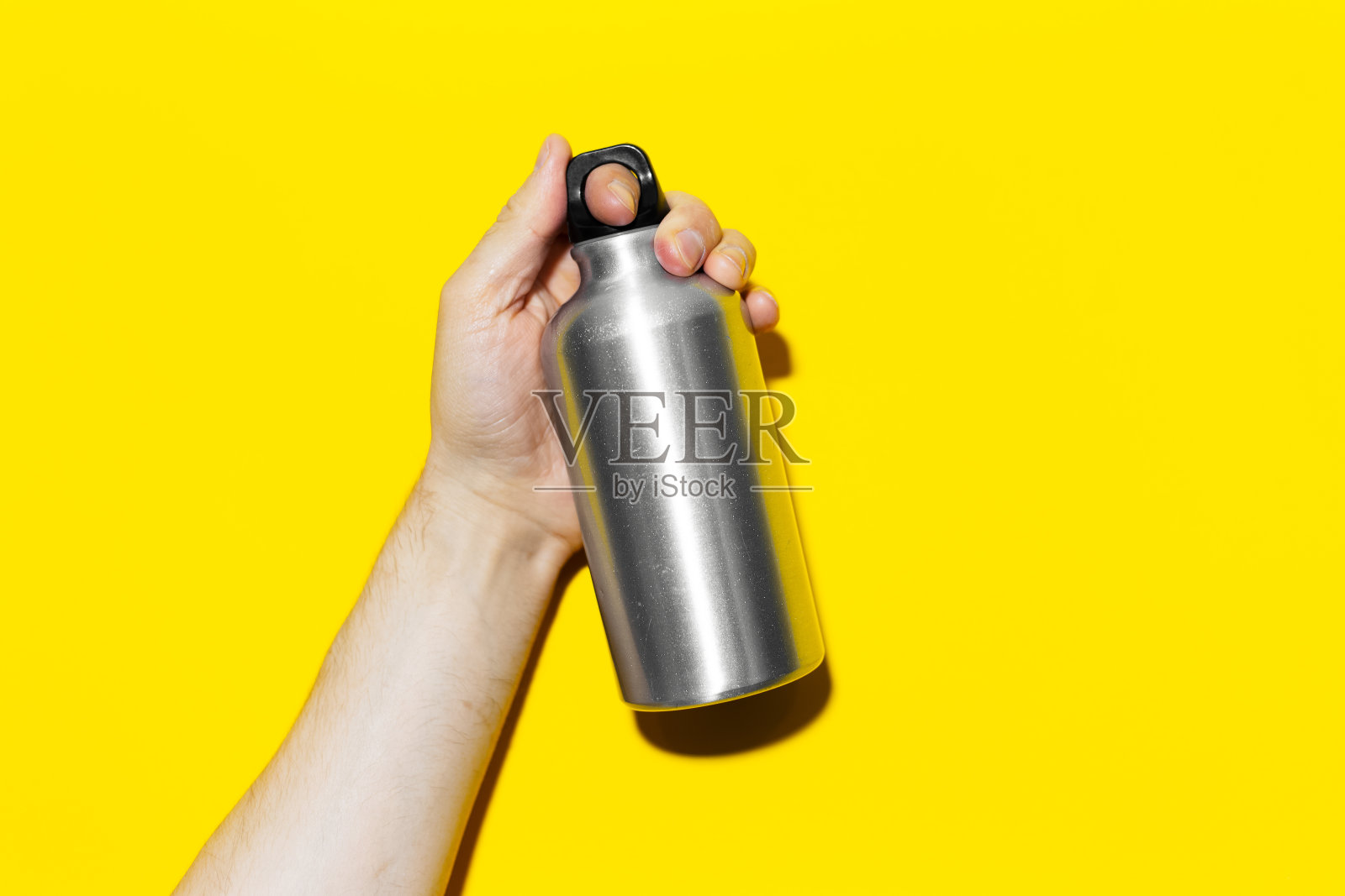 男性的手的特写，拿着铝，热水瓶在黄色的背景。照片摄影图片
