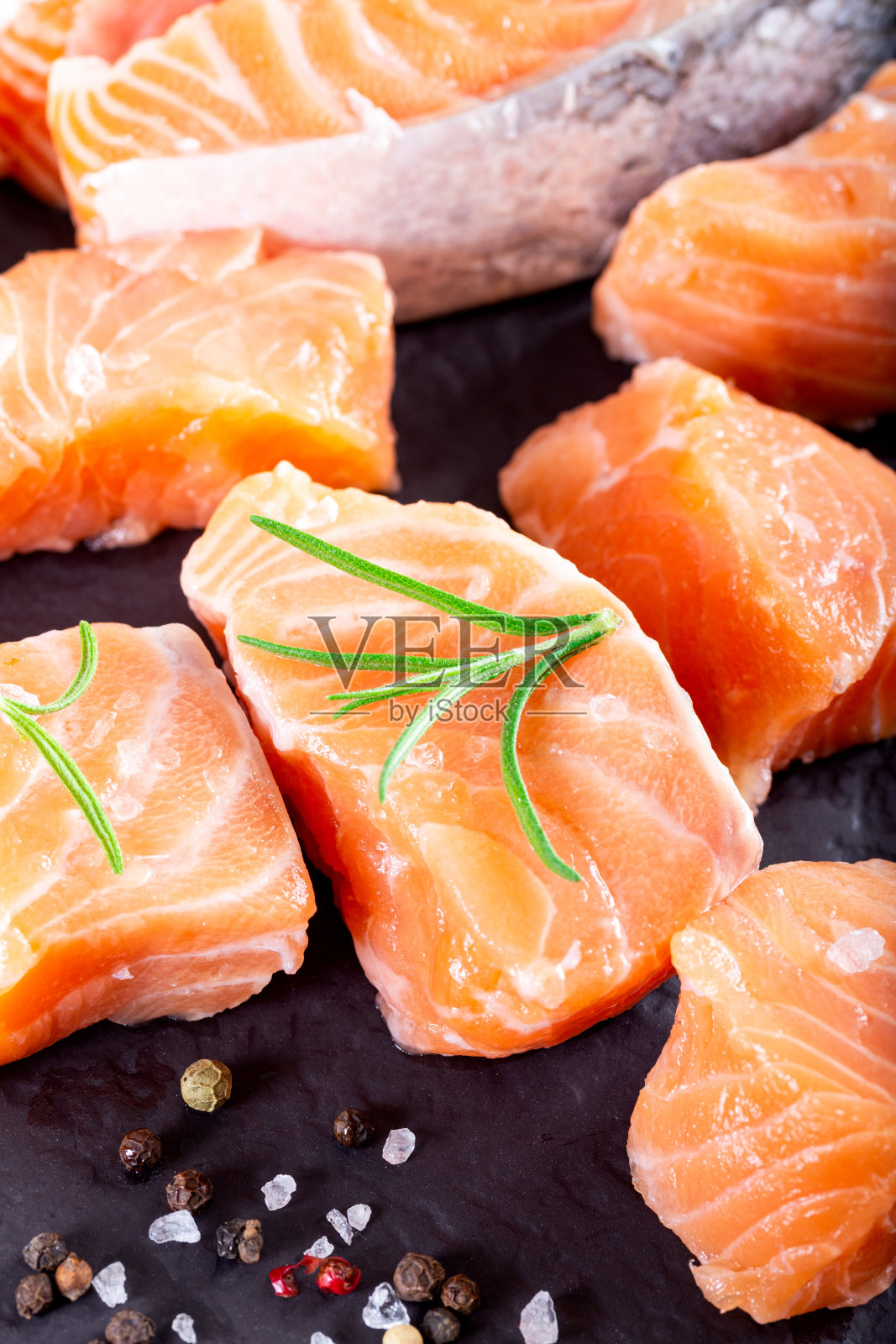 新鲜的三文鱼片放在黑色的切菜板上，加柠檬和香料。健康食品的概念。关闭视图照片摄影图片