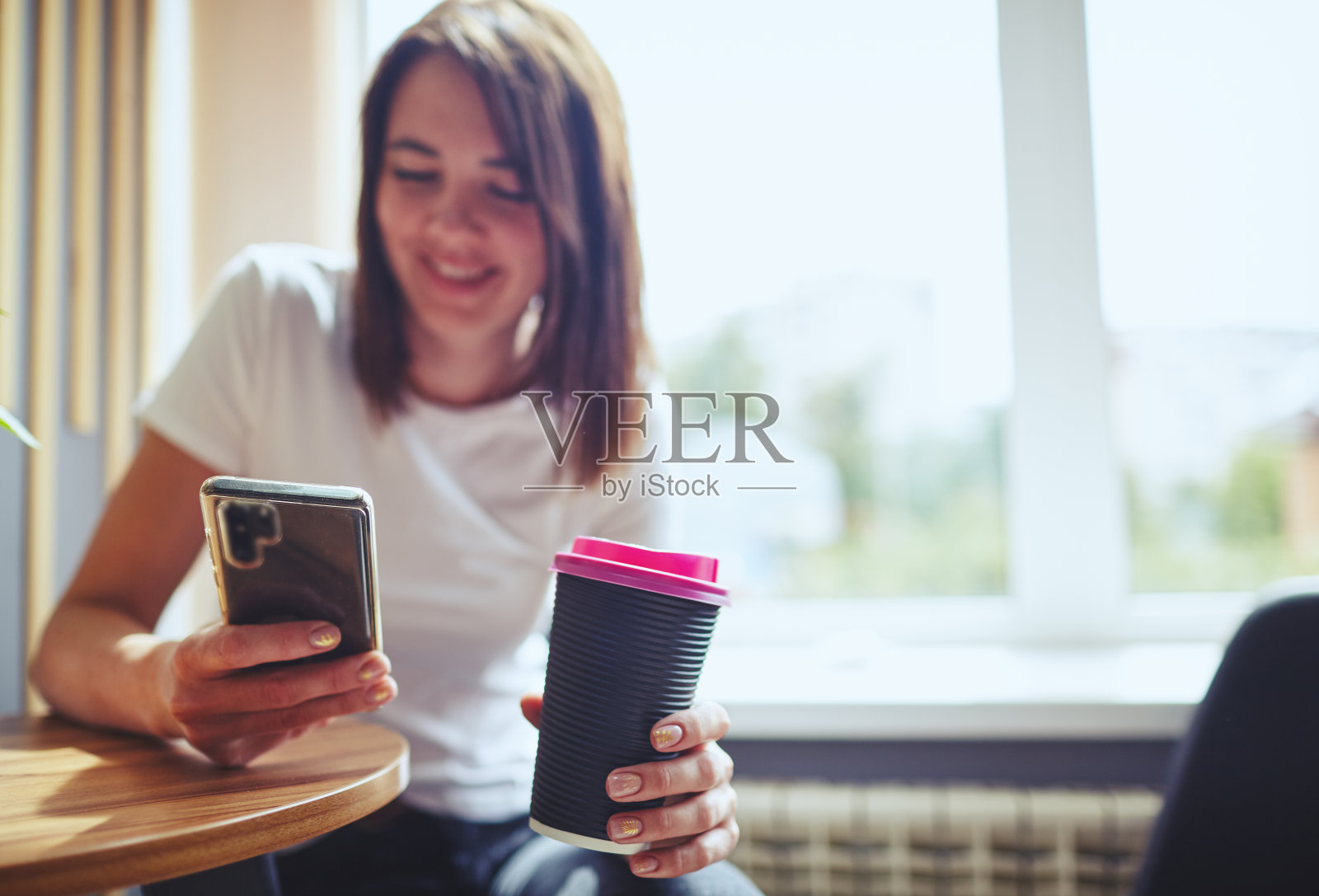 微笑的女人拿着一次性纸杯咖啡和智能手机在咖啡馆。咖啡休息。模糊图像,选择聚焦照片摄影图片
