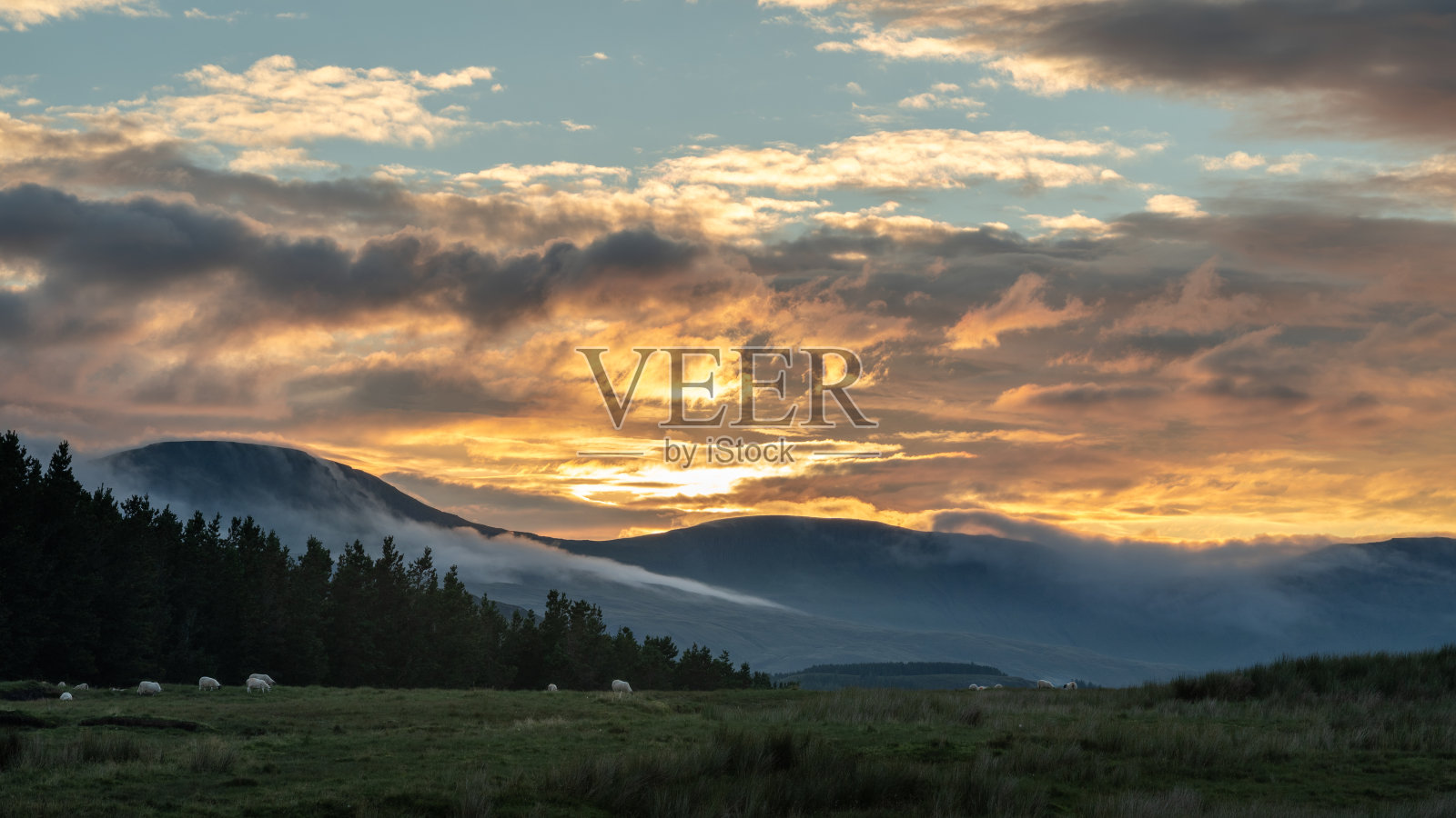 苏格兰斯凯岛的Trotternish山脊全景。美丽的日落在山上与五颜六色的云在天空和薄雾在山上照片摄影图片