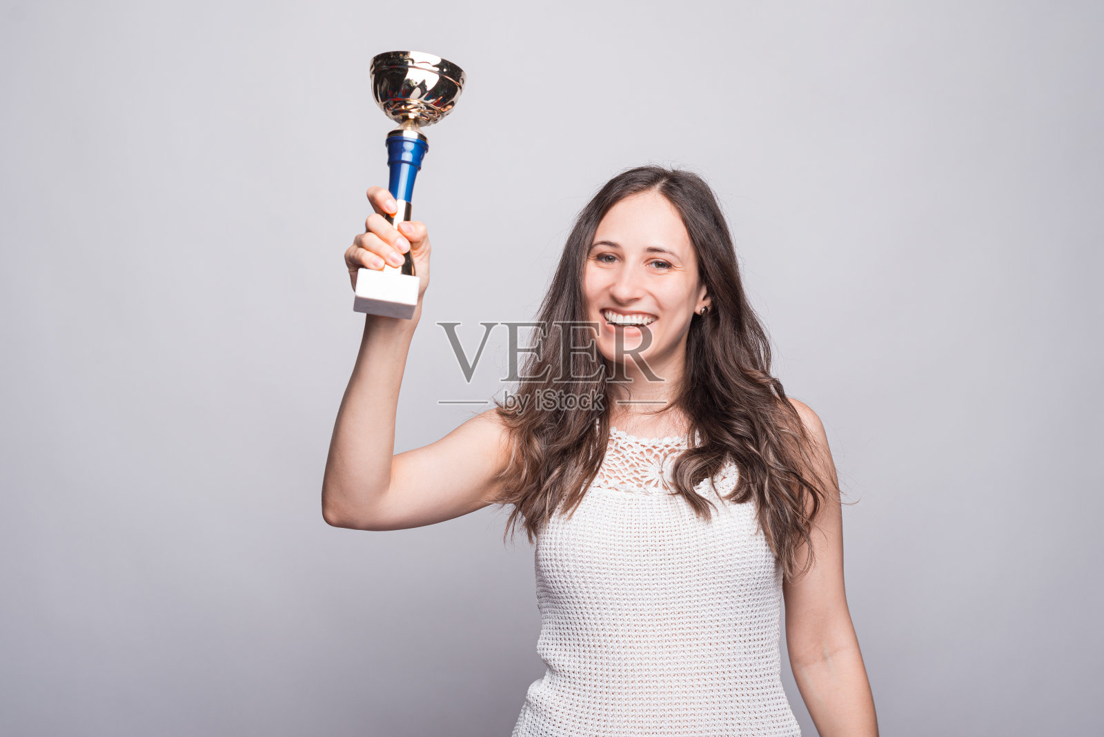 这张照片是一个快乐的年轻女子在庆祝和拿着冠军杯，在镜头前看起来很自信照片摄影图片