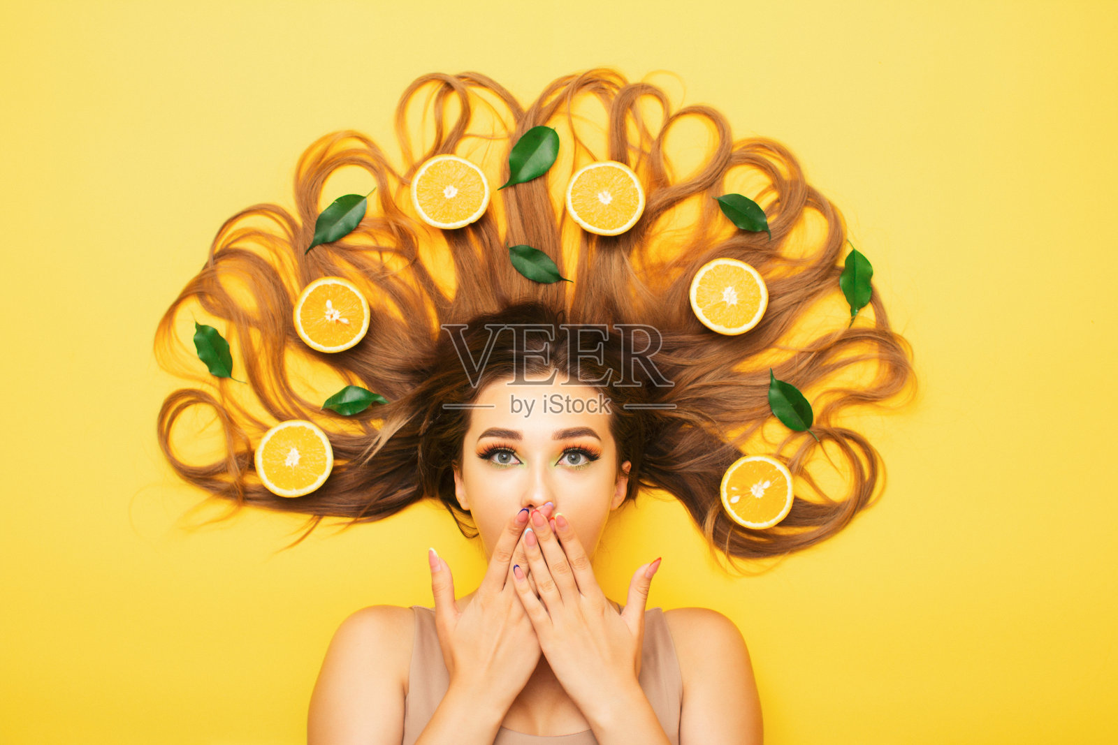 惊奇的女孩躺在桔黄色的长发里，年轻的震惊的女人用柑橘片和叶子，女性的情感照片摄影图片
