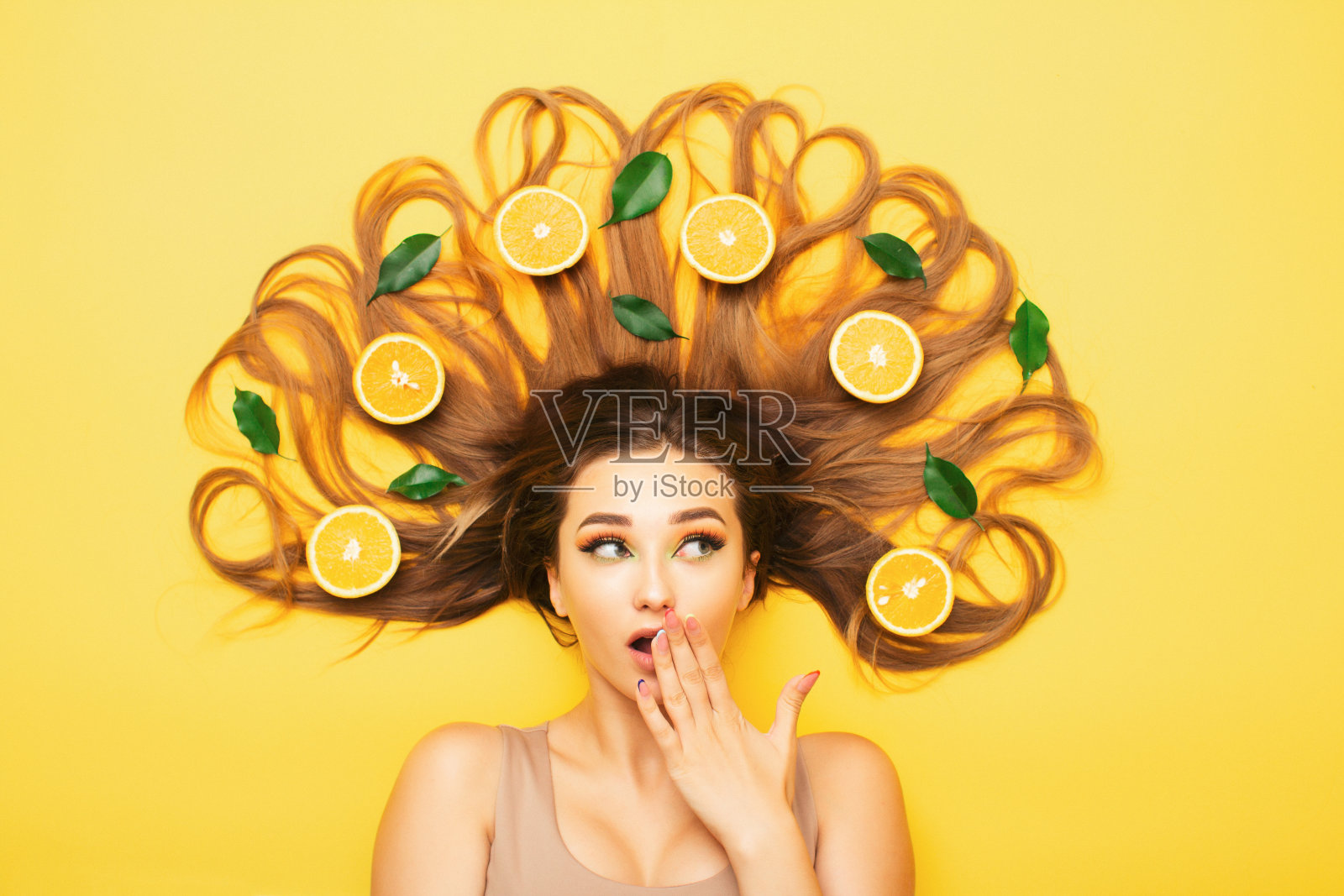惊奇的女孩躺在桔黄色的长发里，年轻的震惊的女人用柑橘片和叶子，女性的情感照片摄影图片