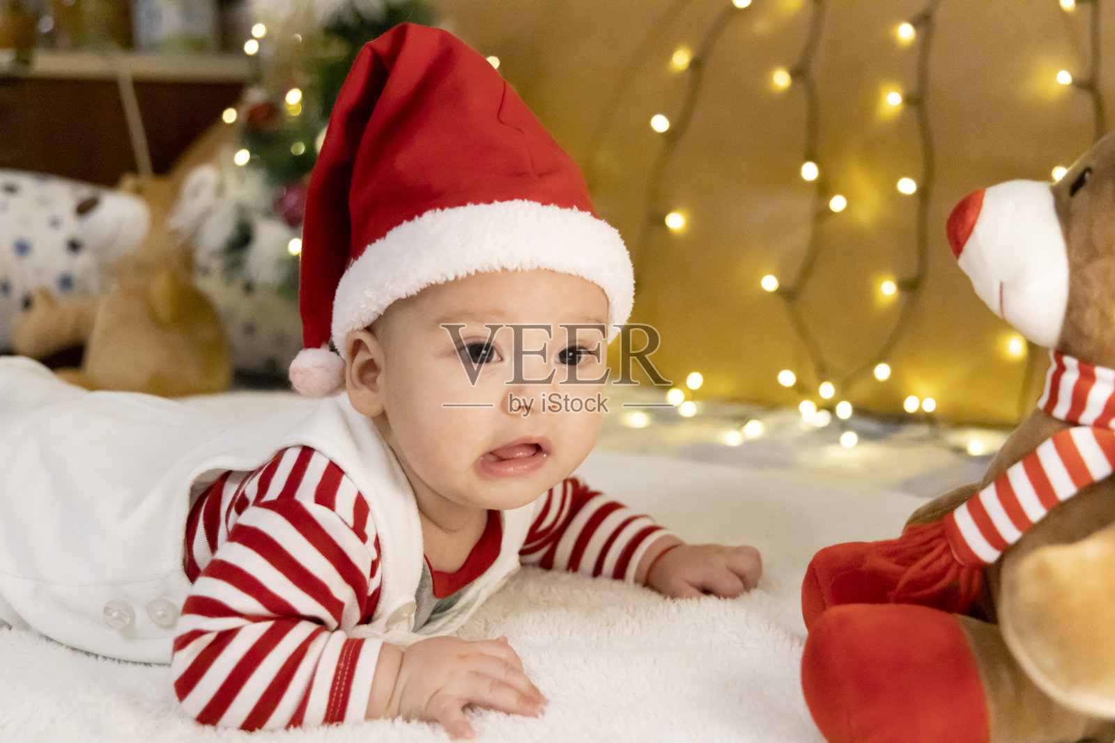 一个戴着圣诞帽的可爱小婴儿躺在羽绒被上。有个小婴儿的圣诞卡片。照片摄影图片