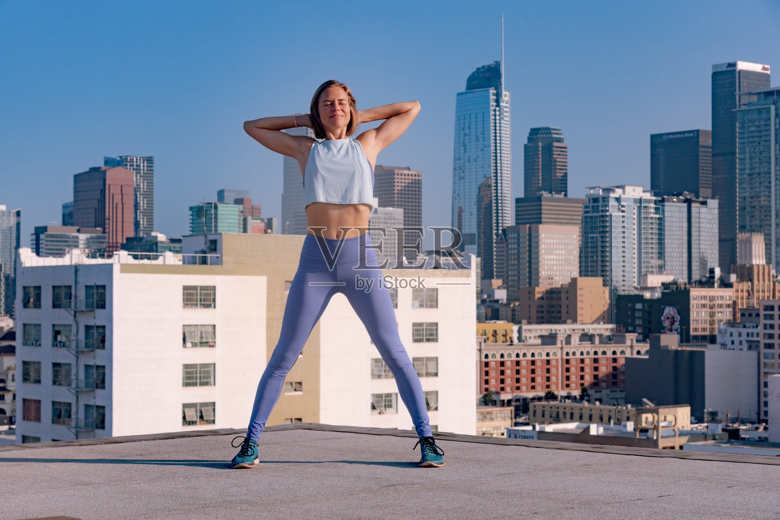 年轻的城市运动员在屋顶上伸展和锻炼，俯瞰洛杉矶市中心照片摄影图片