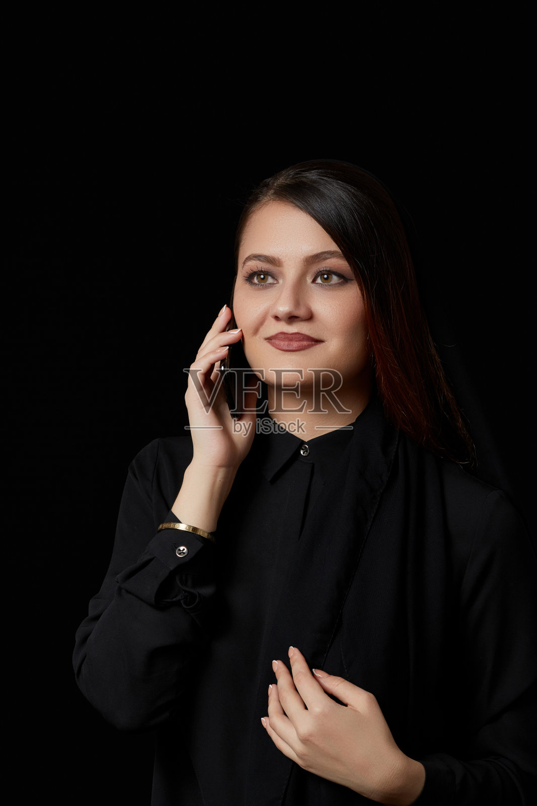 一位身穿黑色衣服的年轻美丽的穆斯林女性正在使用手机，在黑色的独立背景上微笑、发短信、交谈照片摄影图片