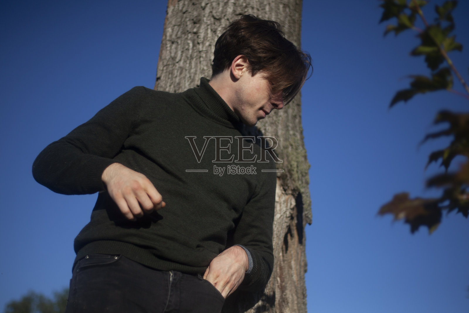 那个人站在一棵树旁。一个穿着半长裙的年轻人。照片摄影图片