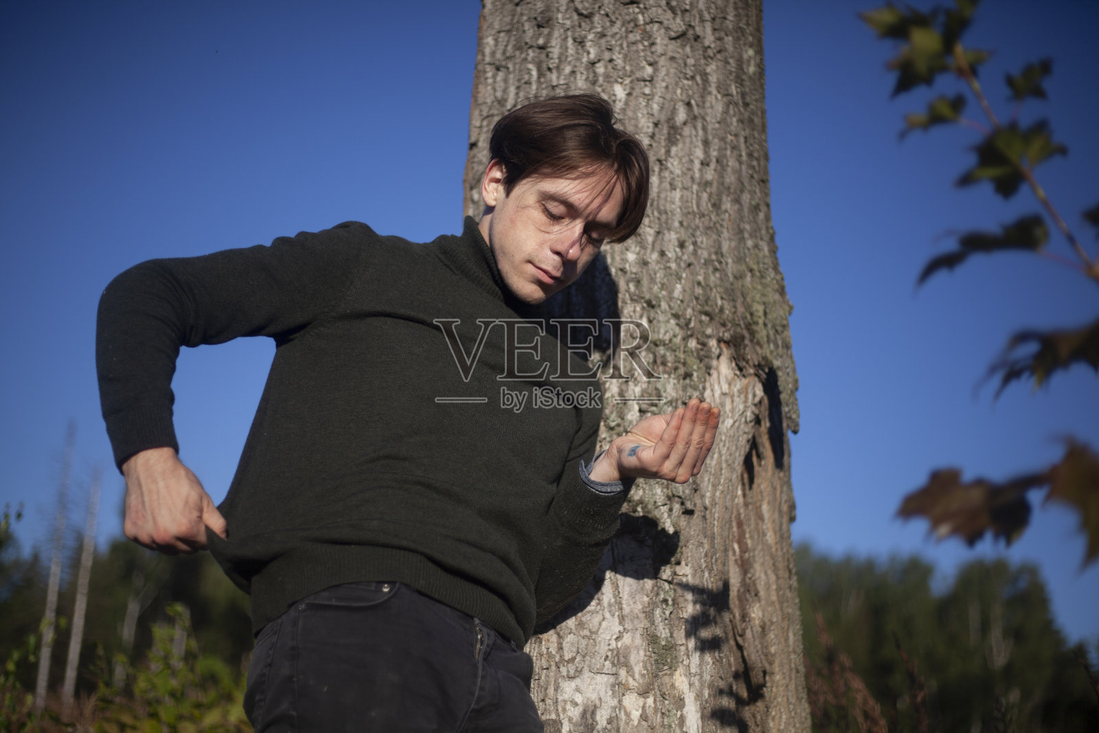 那个人站在一棵树旁。一个穿着半长裙的年轻人。照片摄影图片