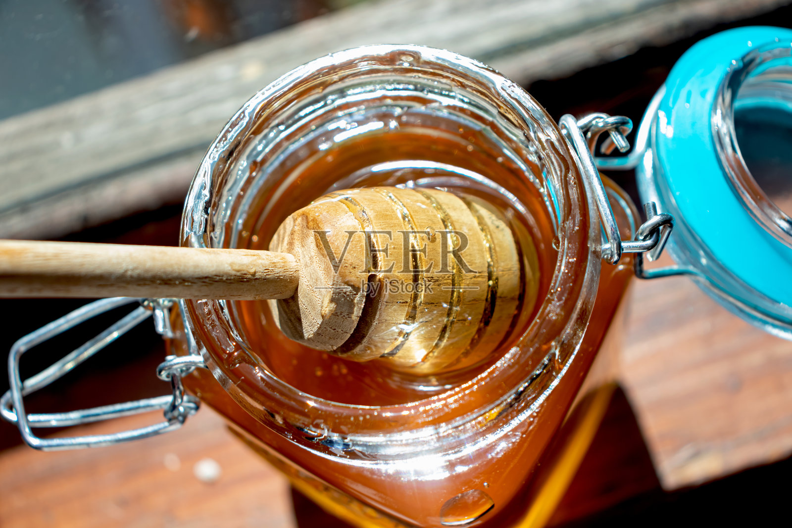 蜂蜜的木棒躺在一罐金黄色的阳光甜甜的蜂蜜里。窗台上放着一个玻璃罐照片摄影图片
