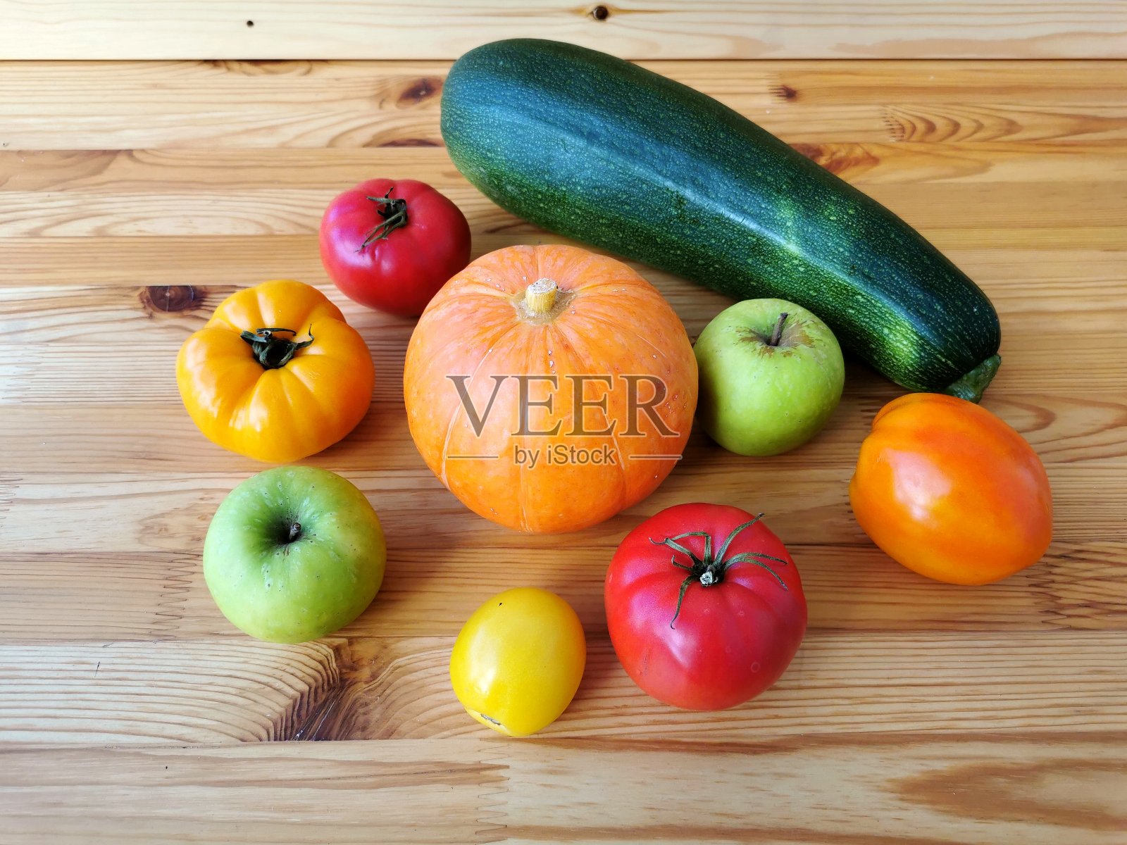 木桌上放着南瓜、五颜六色的西红柿、苹果和西葫芦照片摄影图片