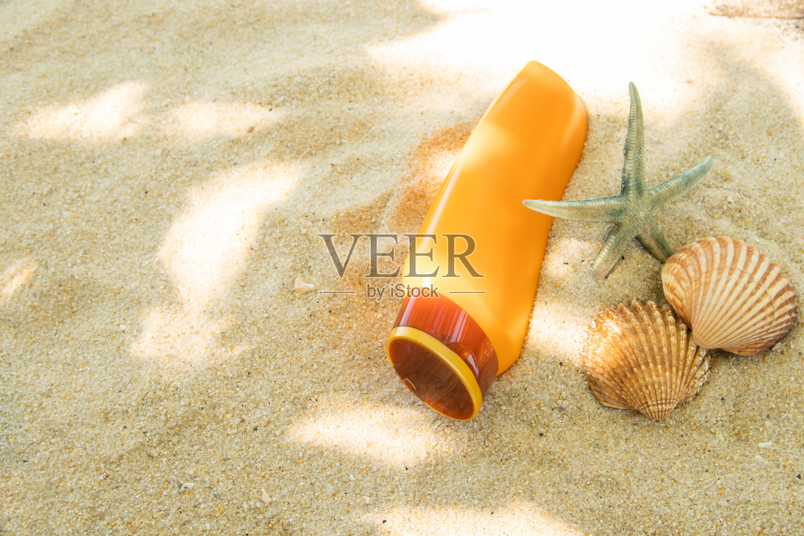 一瓶防晒油或防晒霜放在沙滩上，上面有海贝照片摄影图片