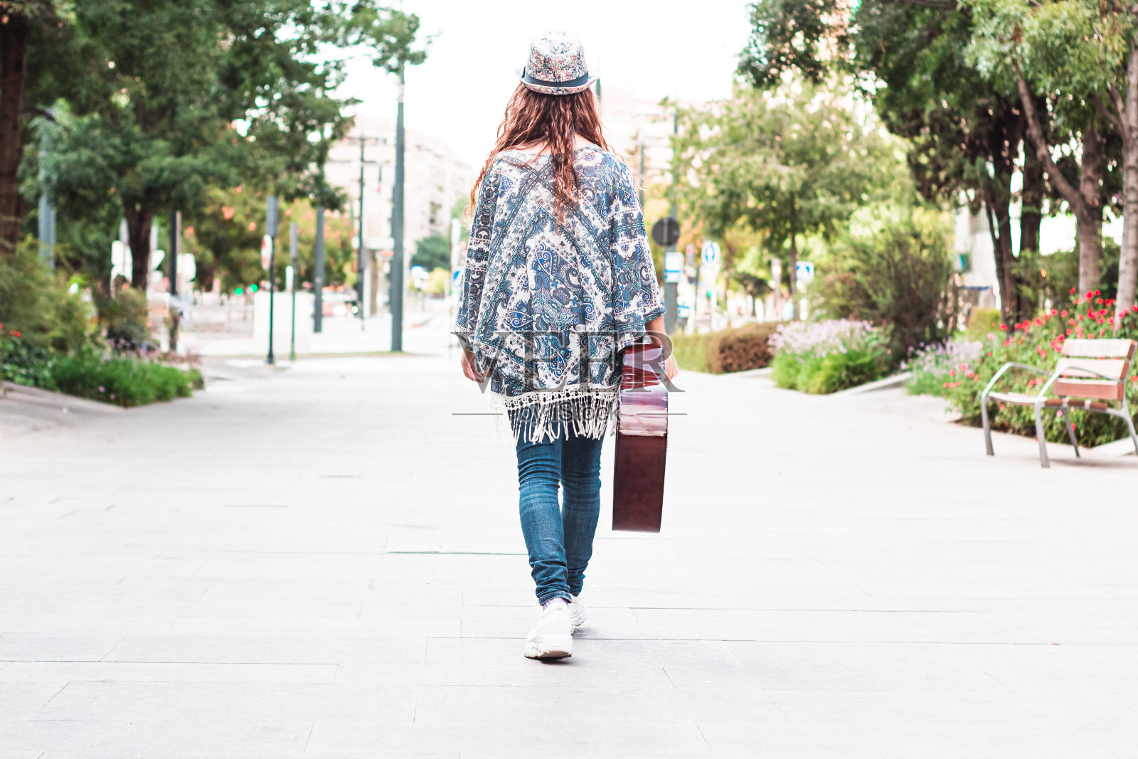 年轻的现代女性手里拿着吉他走在街上。照片摄影图片